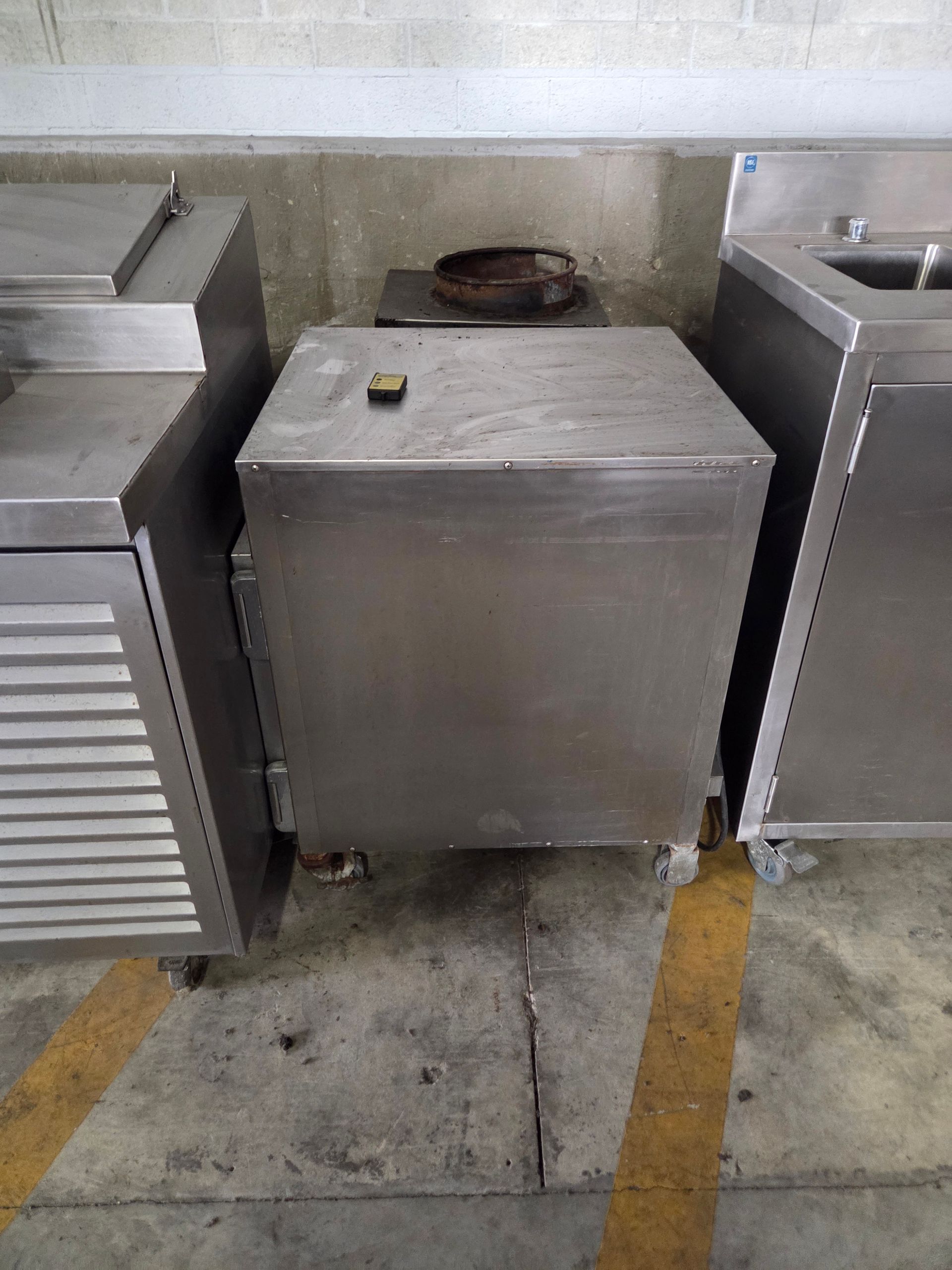 Stainless steel commercial kitchen equipment, including a boxy refrigerator and sinks.