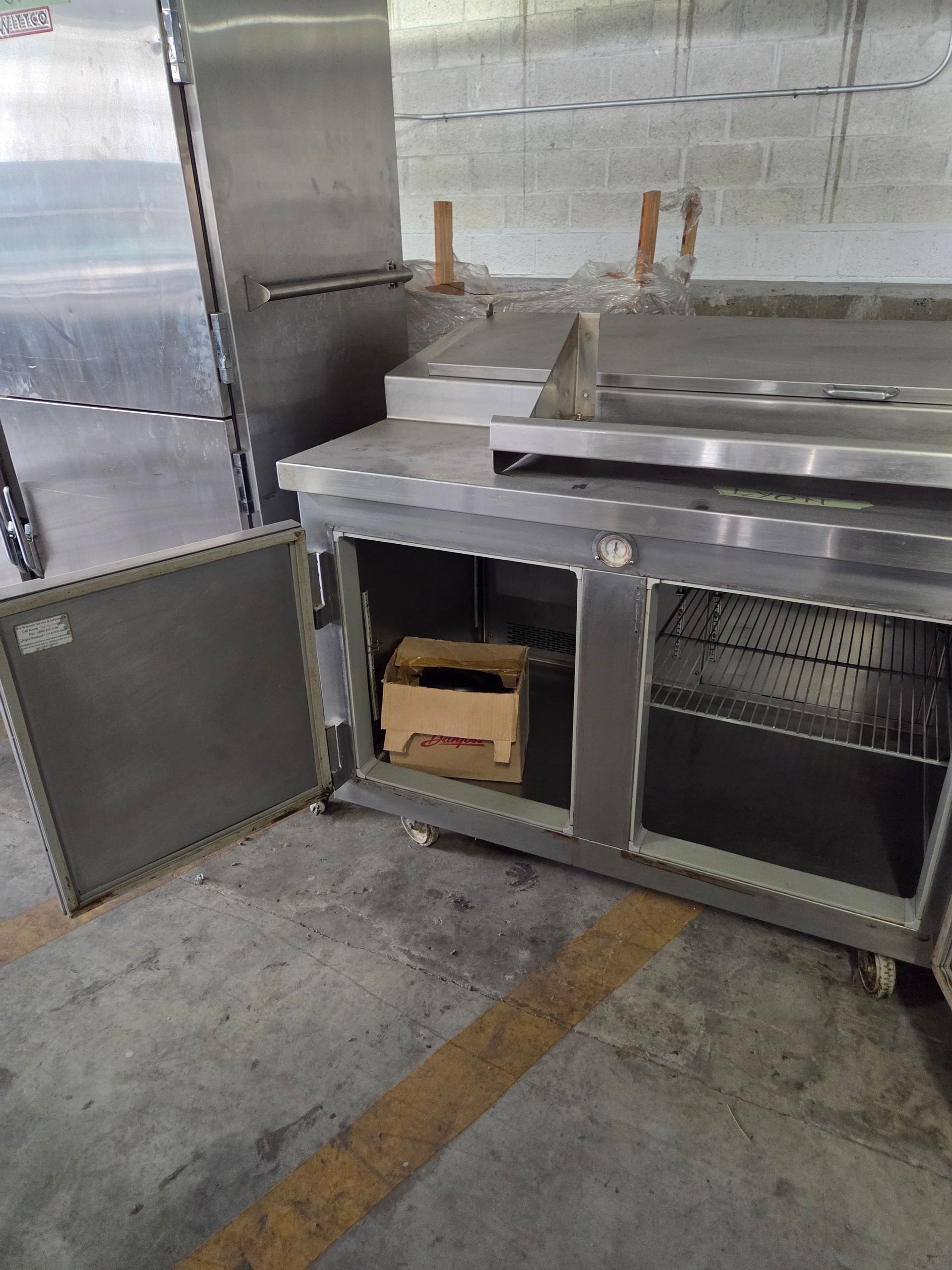 Stainless steel commercial refrigerator with open door revealing interior and shelf.
