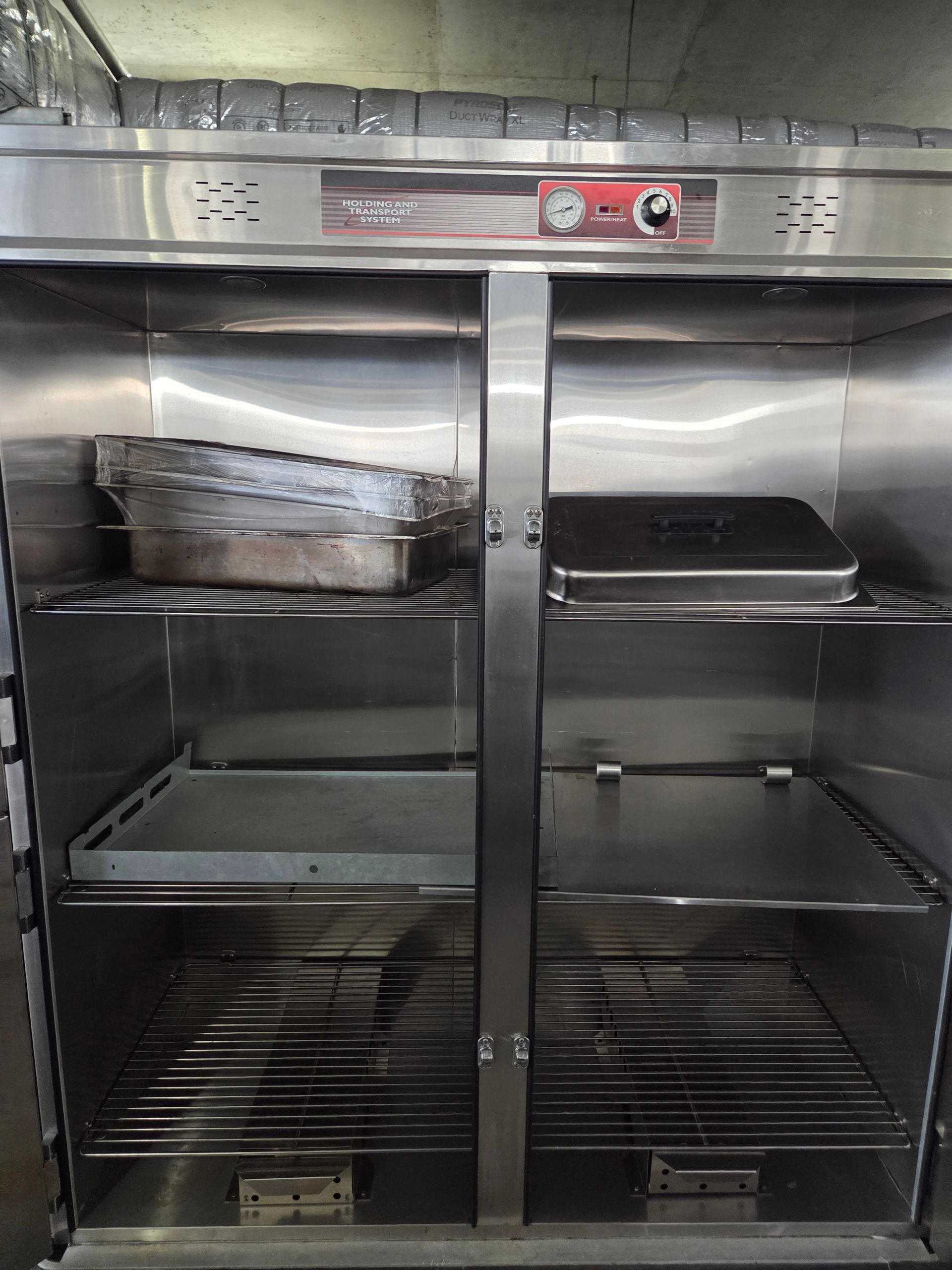 Stainless steel commercial food warmer with open doors, holding trays.