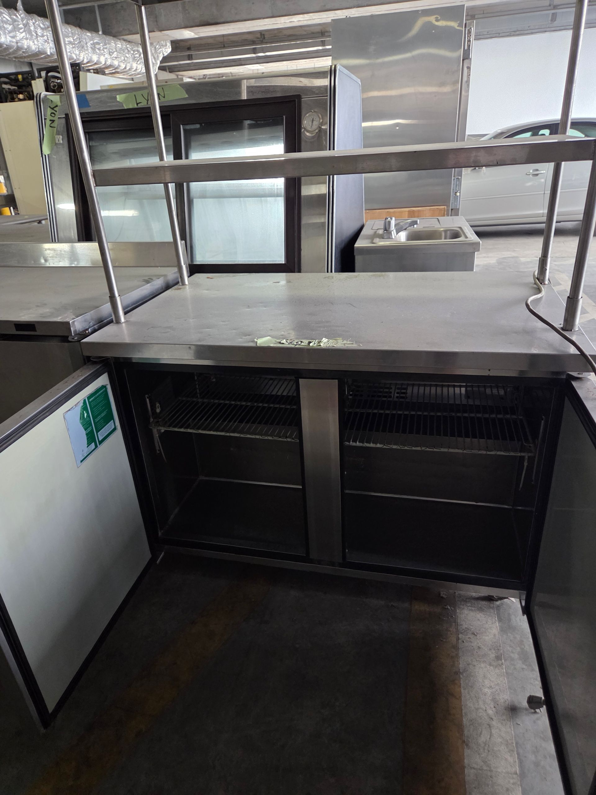 Stainless steel commercial refrigerator with open doors, shelves, and overhead bar in a kitchen.