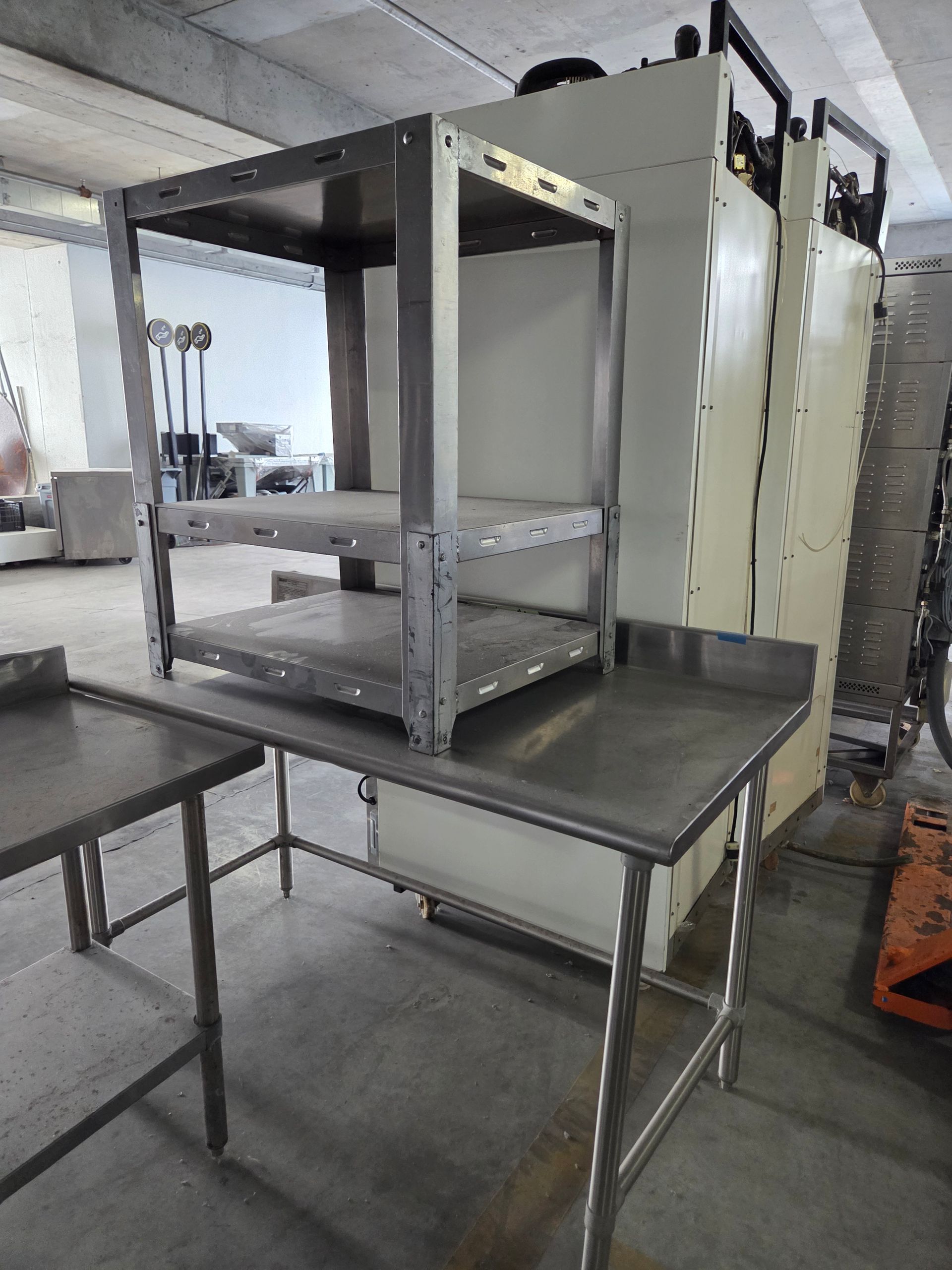 Stainless steel shelving unit on a stainless steel table, near other industrial equipment in a warehouse.