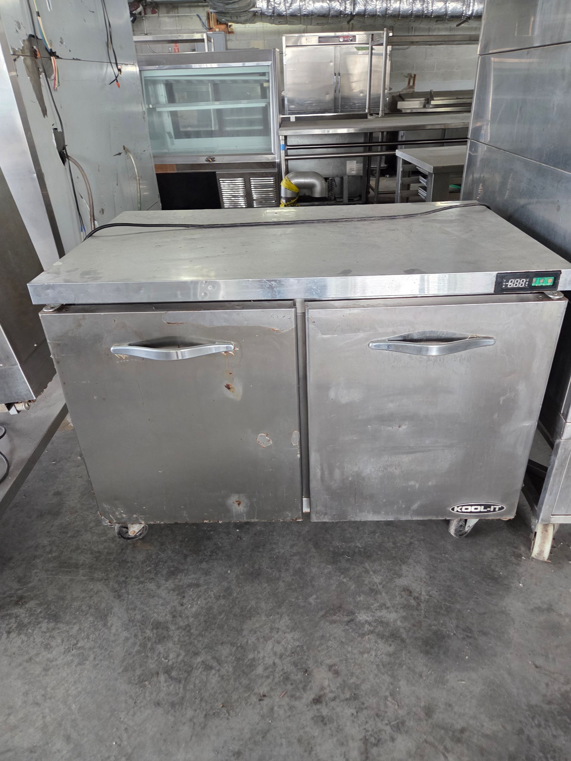 Stainless steel two-door commercial refrigerator on wheels, in a kitchen setting.