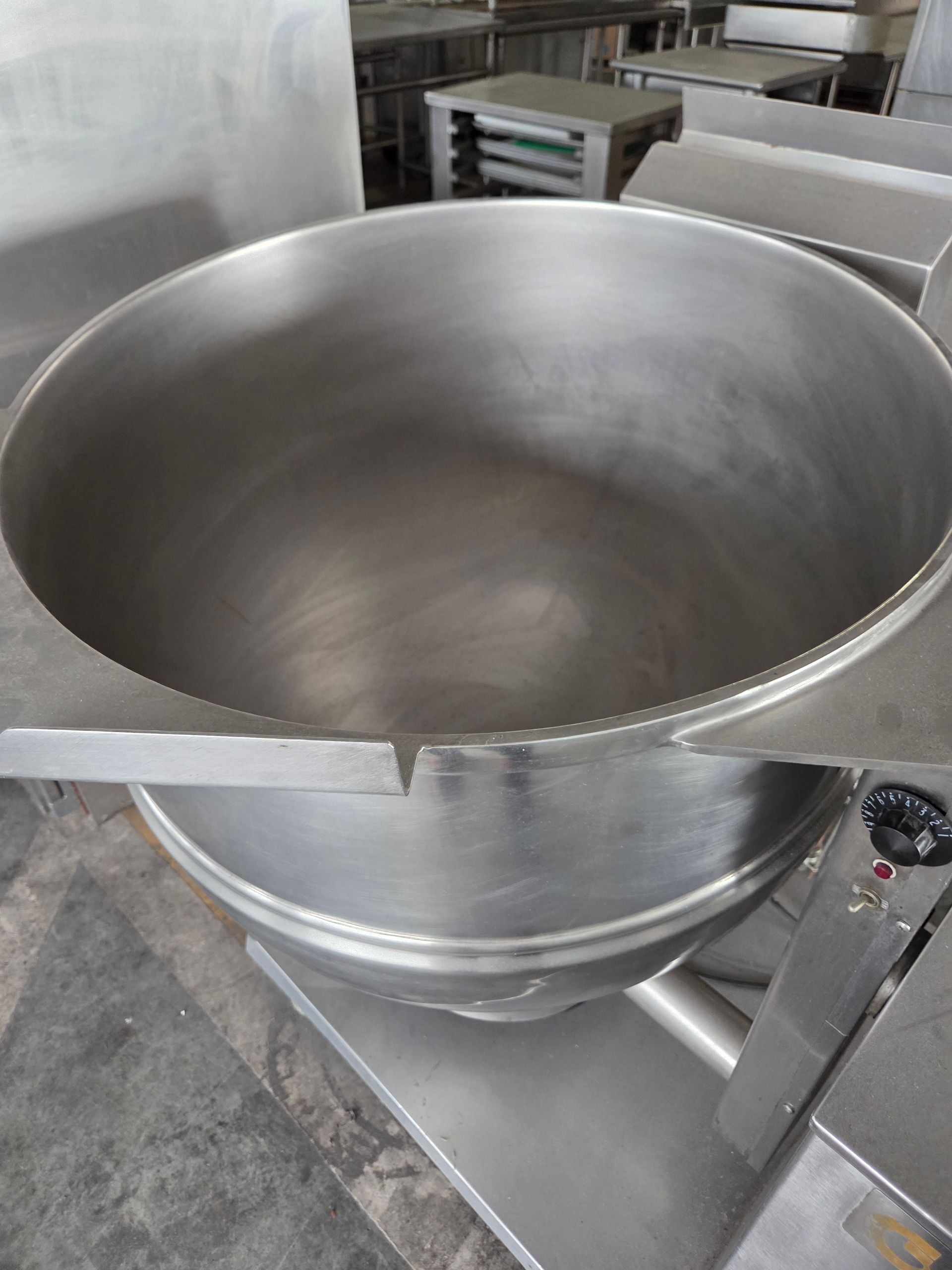 Large stainless steel commercial cooking pot, empty, in a kitchen setting.
