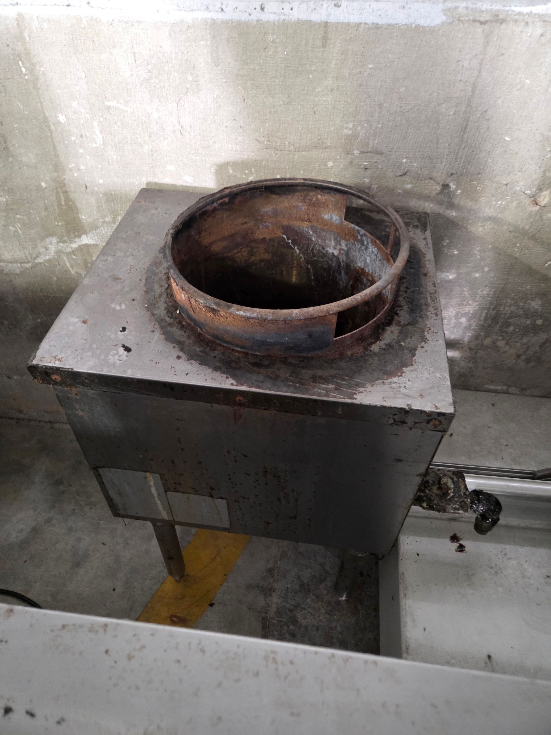 Metal industrial cooking appliance. Has a rusted circular inset on a square metal surface.