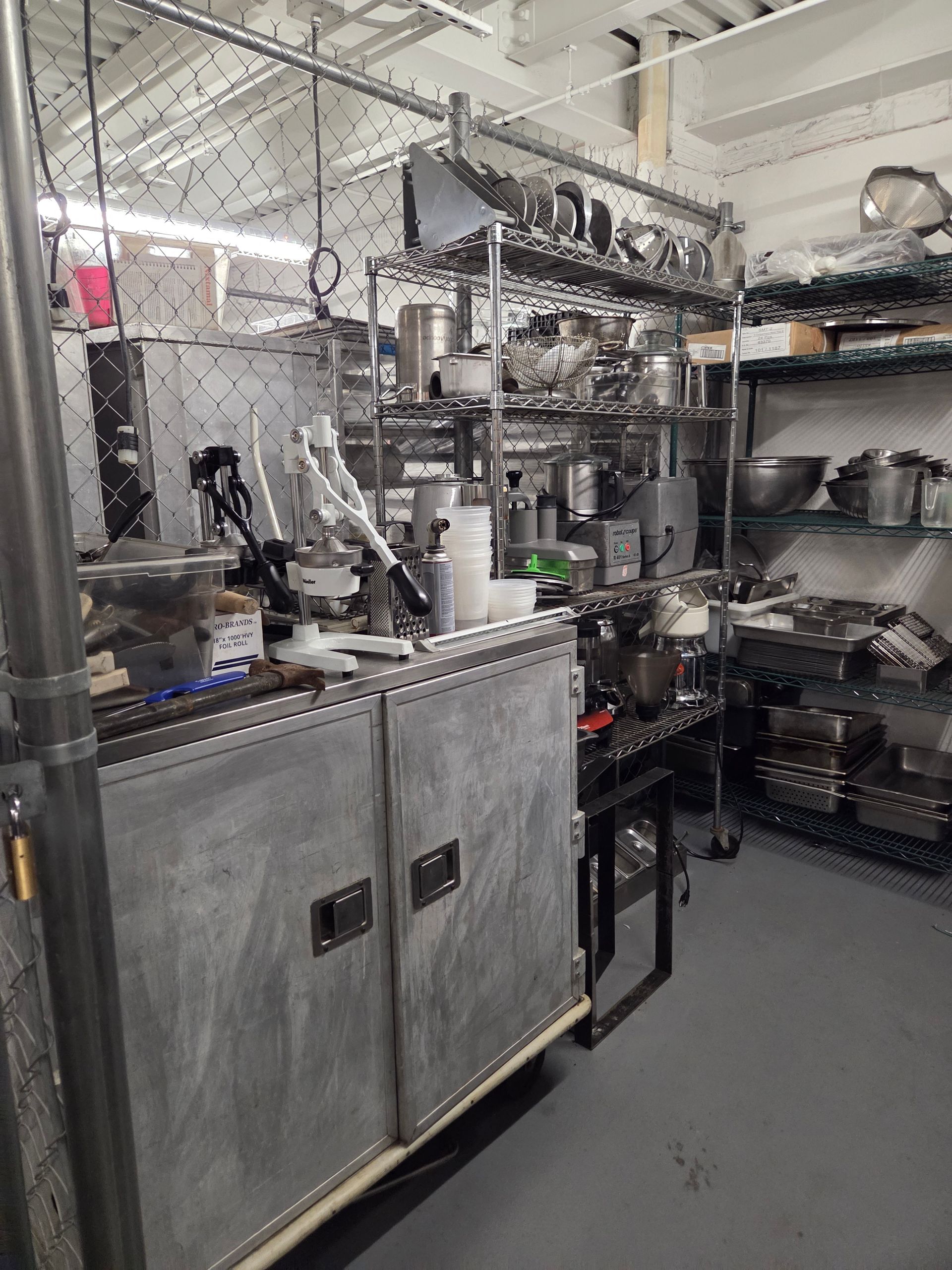 Kitchen with metal shelving, appliances, and cabinetry. Utensils and equipment visible.