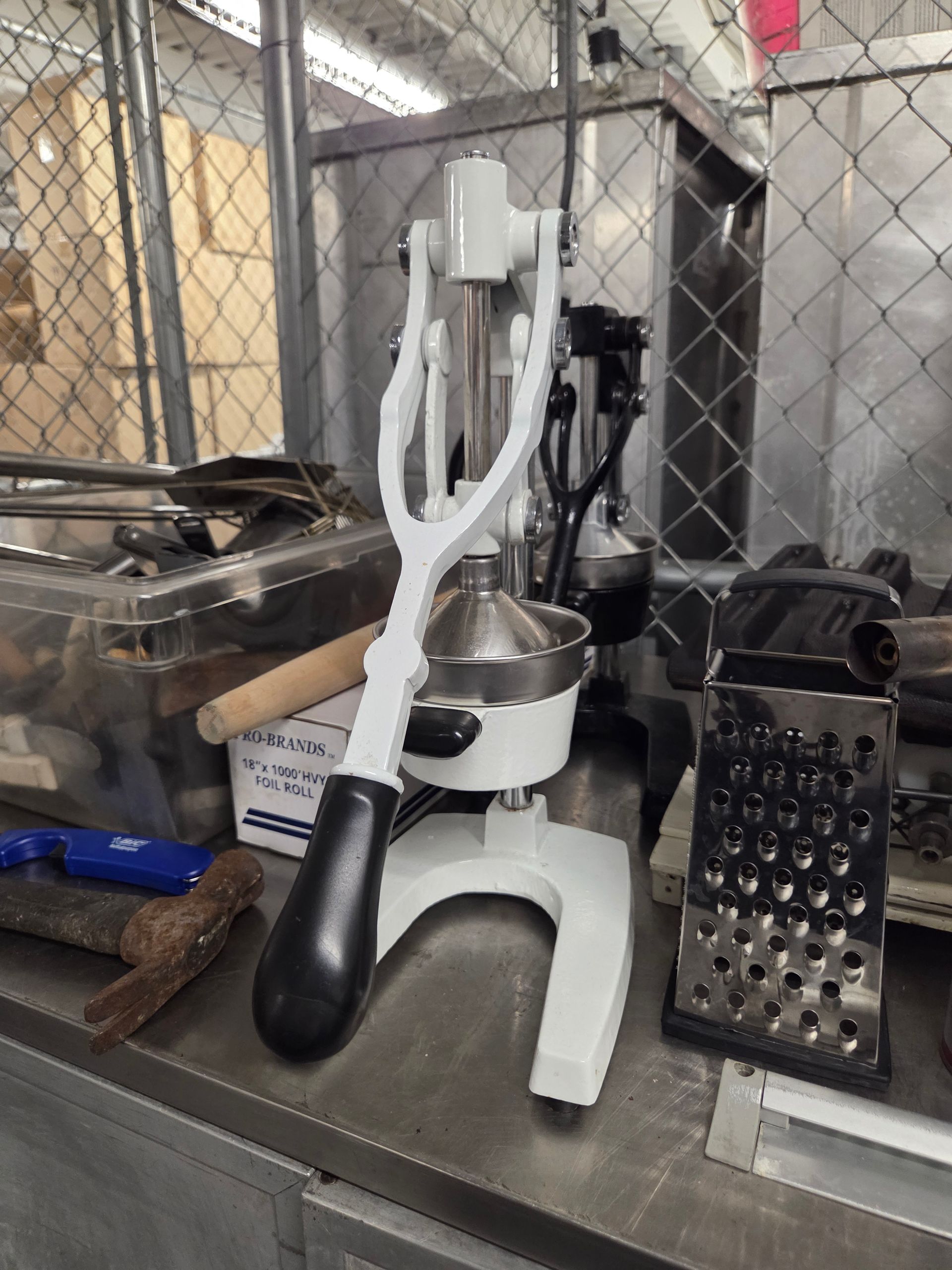White citrus juicer on a metal table, with a black handle. Grater and tools nearby.