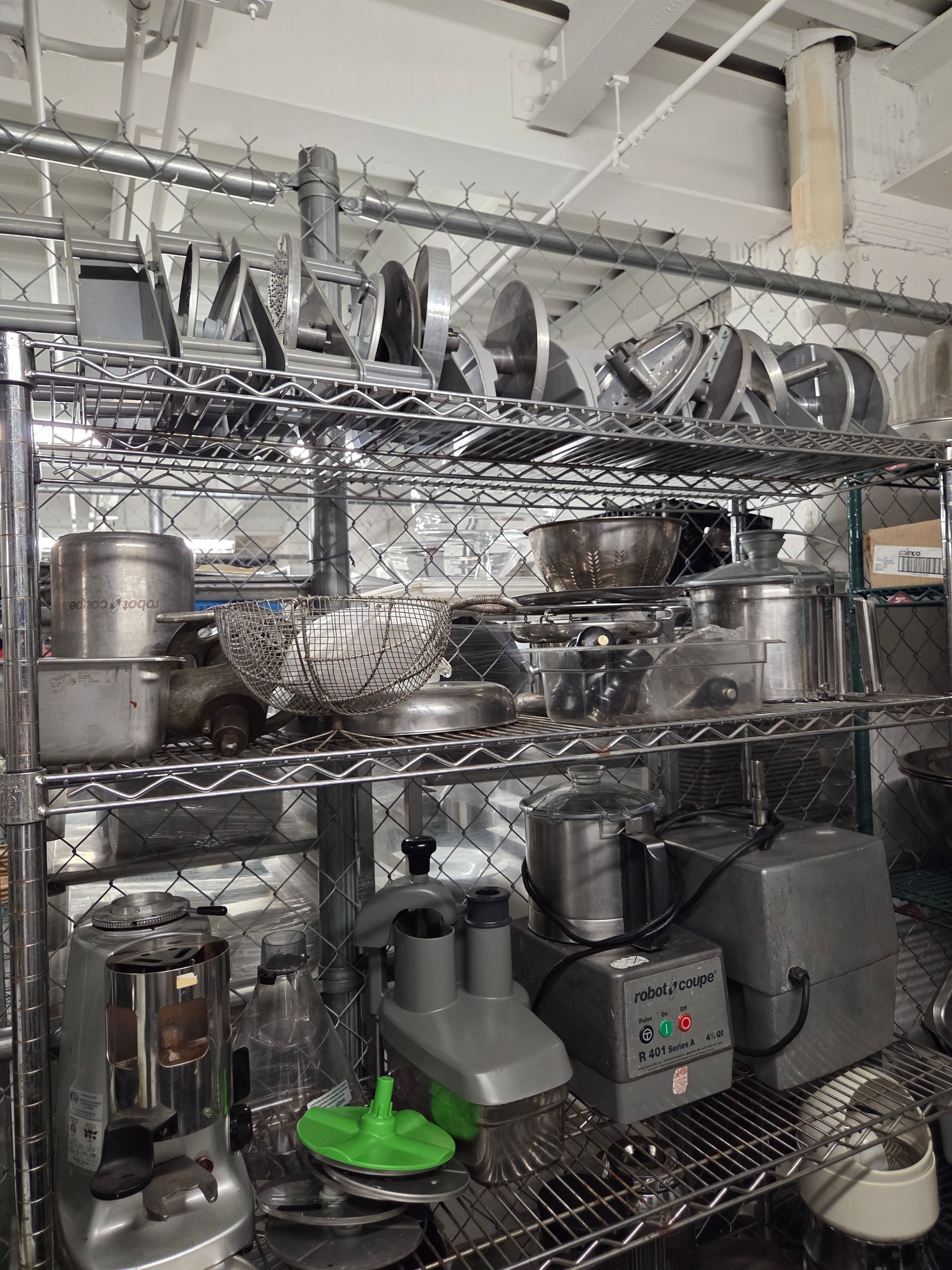 Metal shelving unit in a kitchen filled with pots, pans, and food processing equipment.