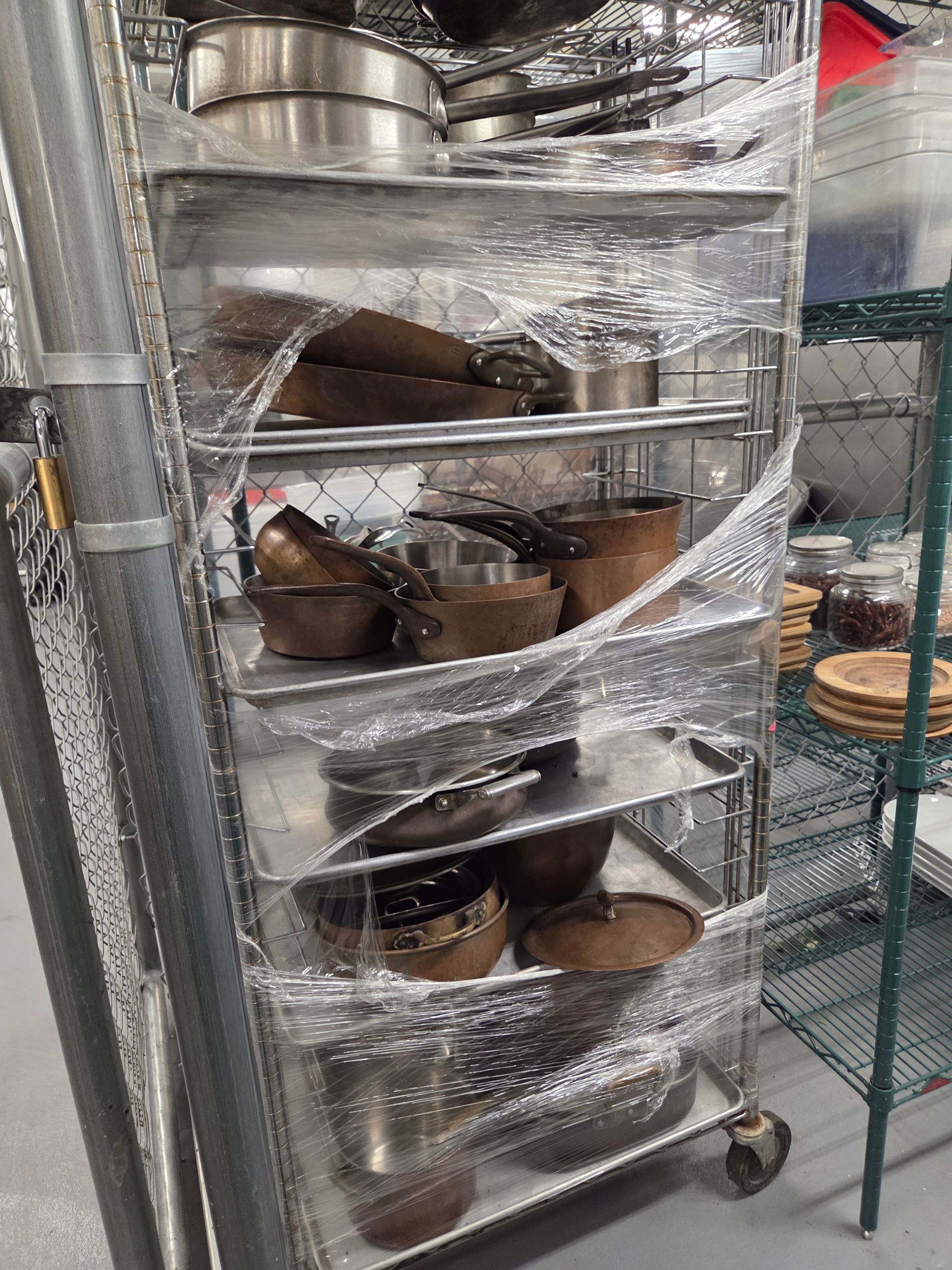 A metal rack with various pots and pans, wrapped in plastic, sitting indoors.
