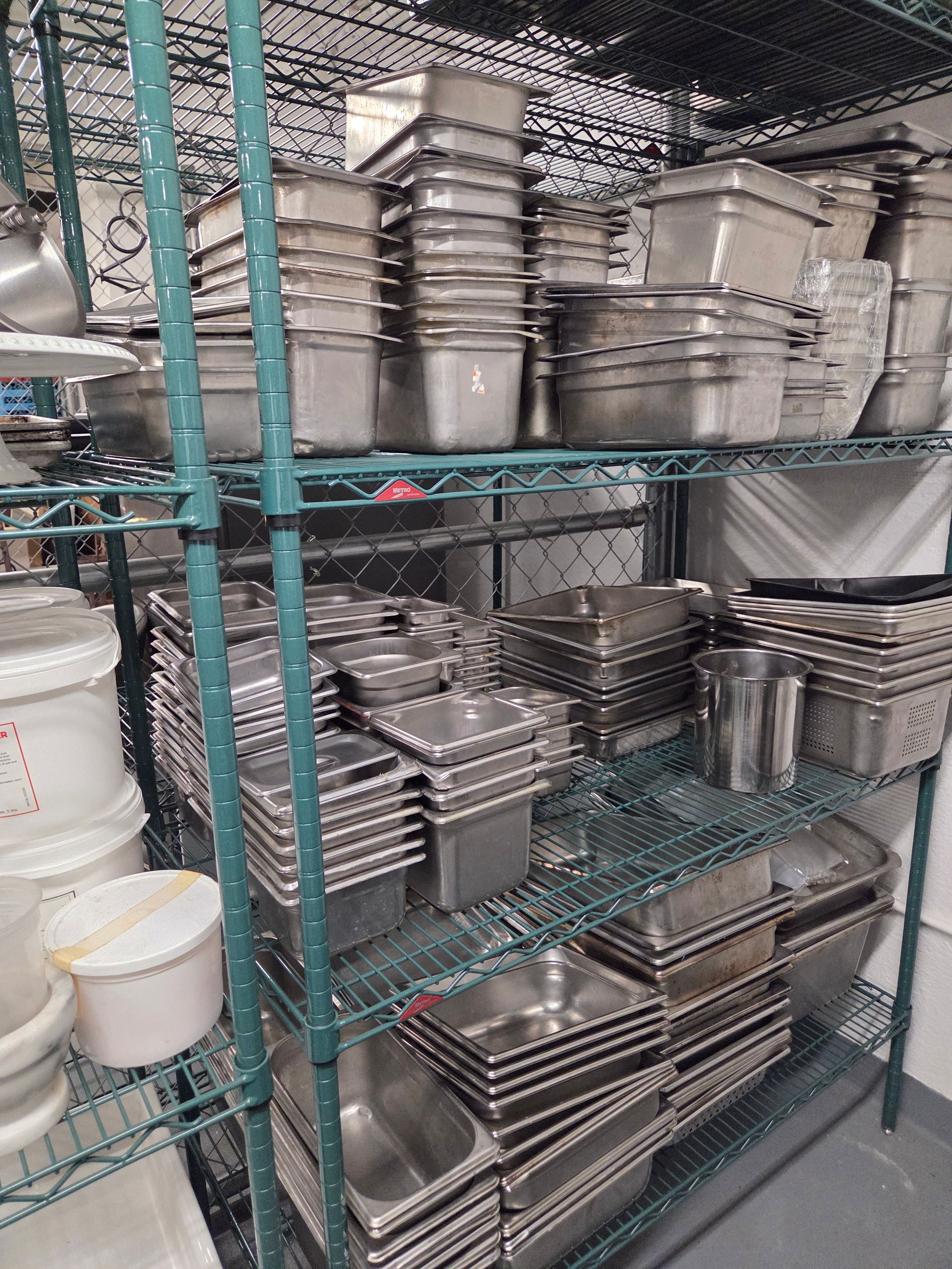 Metal food storage containers stacked on wire shelving in a kitchen.