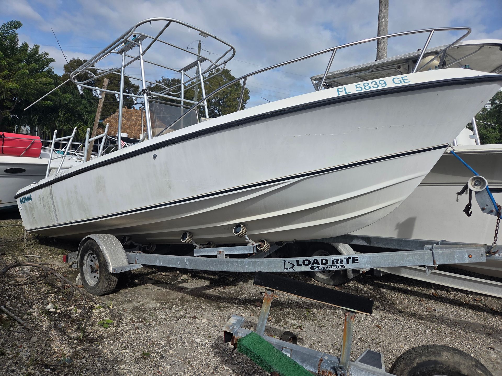 White boat on a trailer, parked on land. Metal frame overhead, blue Florida registration.