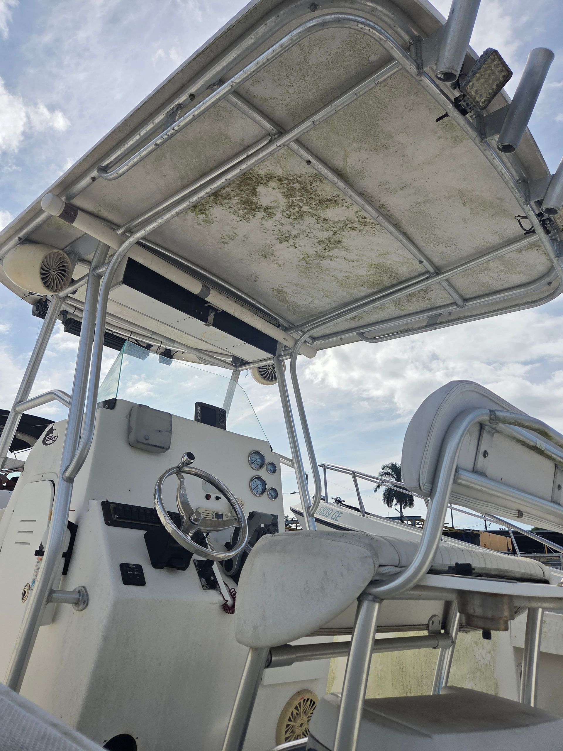 Boat cabin with a weathered, algae-covered top, steering wheel, and seating.