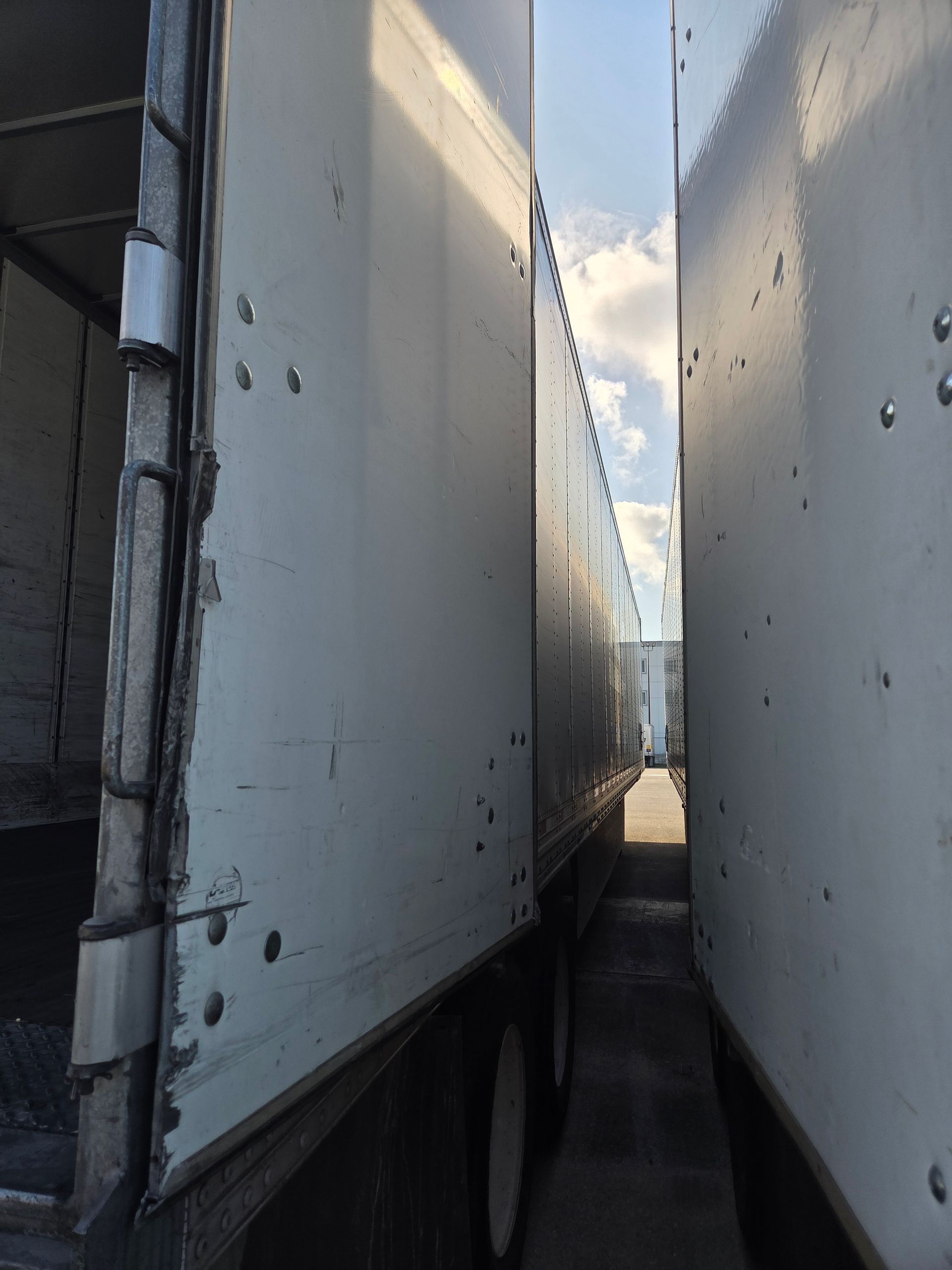Two white semi-truck trailers parked close together, with narrow passage between them.