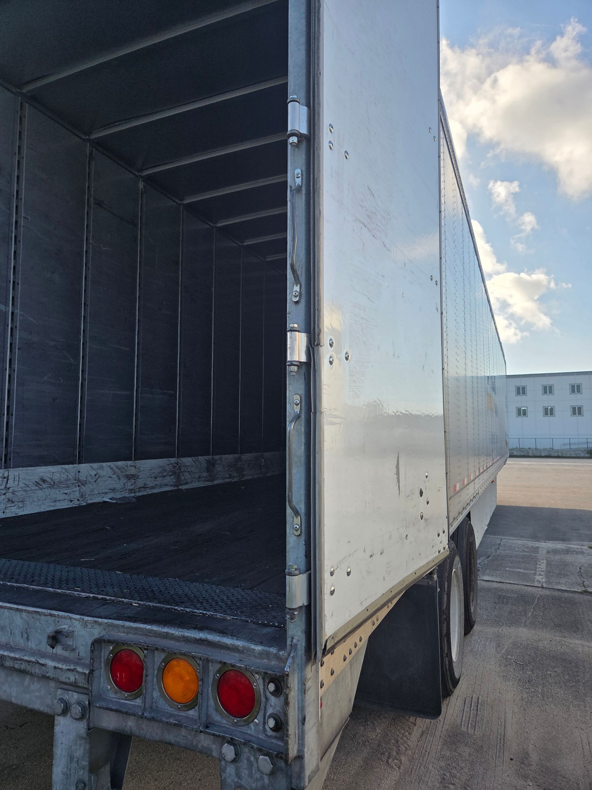 Open, empty white semi-trailer with taillights, parked outside on a cloudy day.