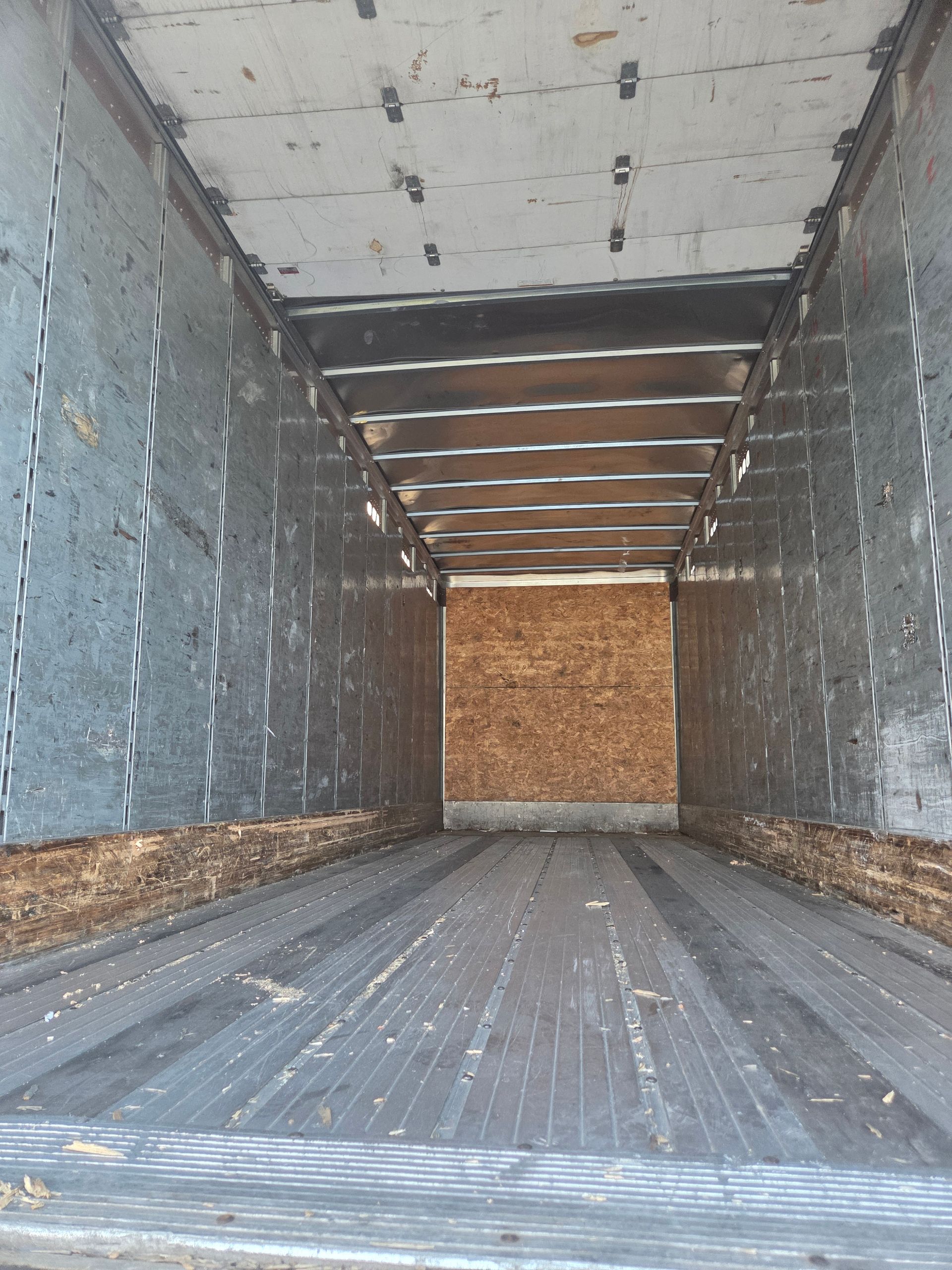 Interior of an empty semi-truck trailer, with wood floor and walls, metal ceiling, and plywood bulkhead.
