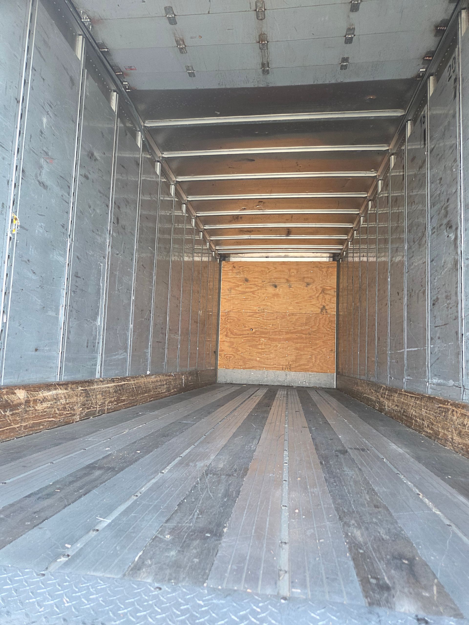 Interior of an empty semi-truck cargo area. Metal walls and ceiling, wood floor, and back wall.