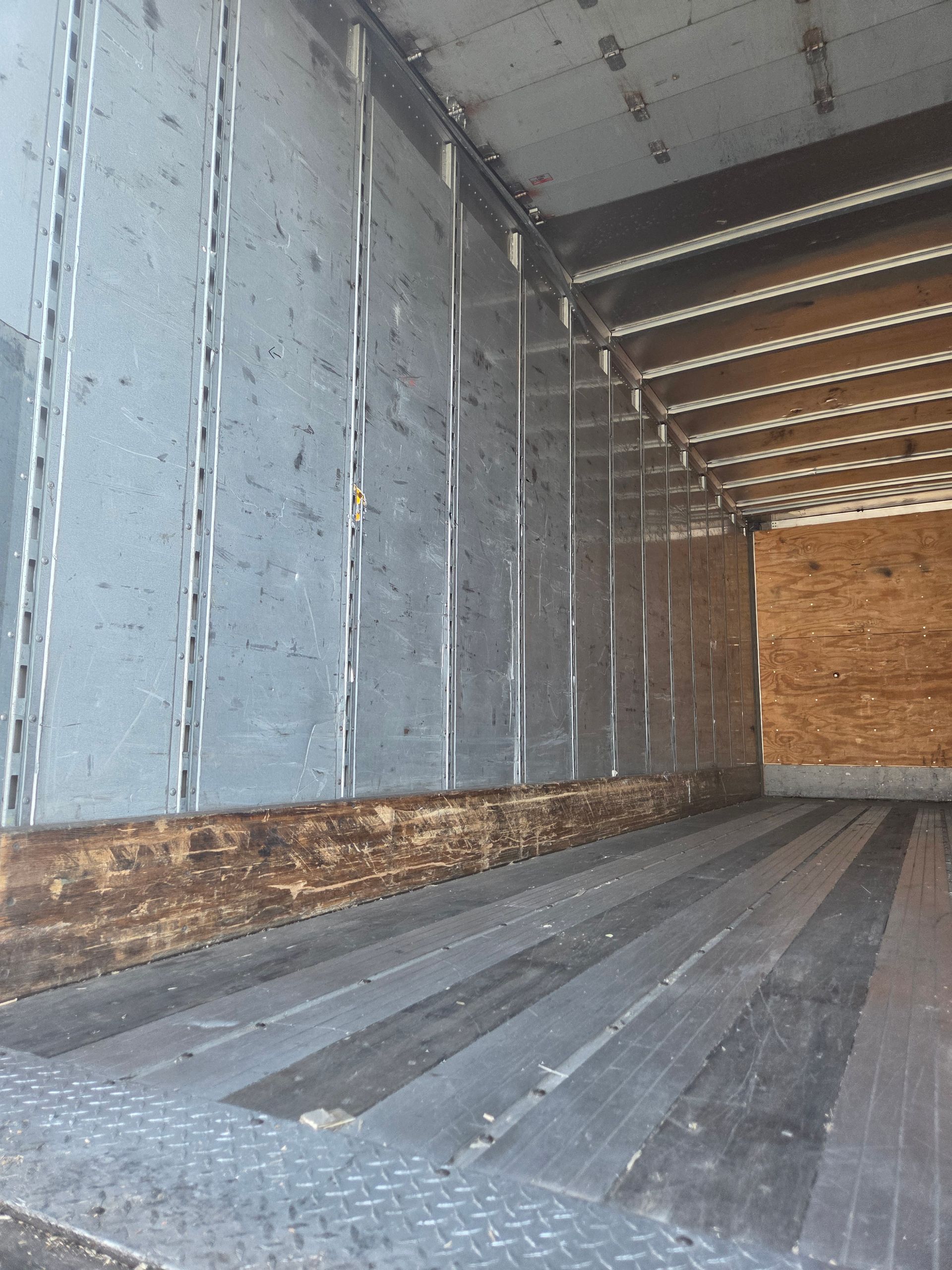 Interior of a cargo truck. Gray corrugated floor, metal side paneling, wood paneling at the back.
