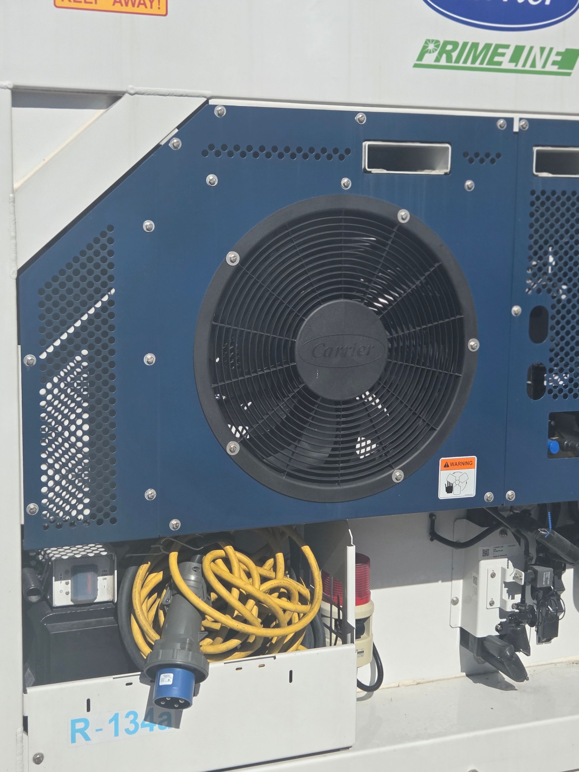Close-up of a blue and white refrigerated trailer unit with a black fan and electrical cords.