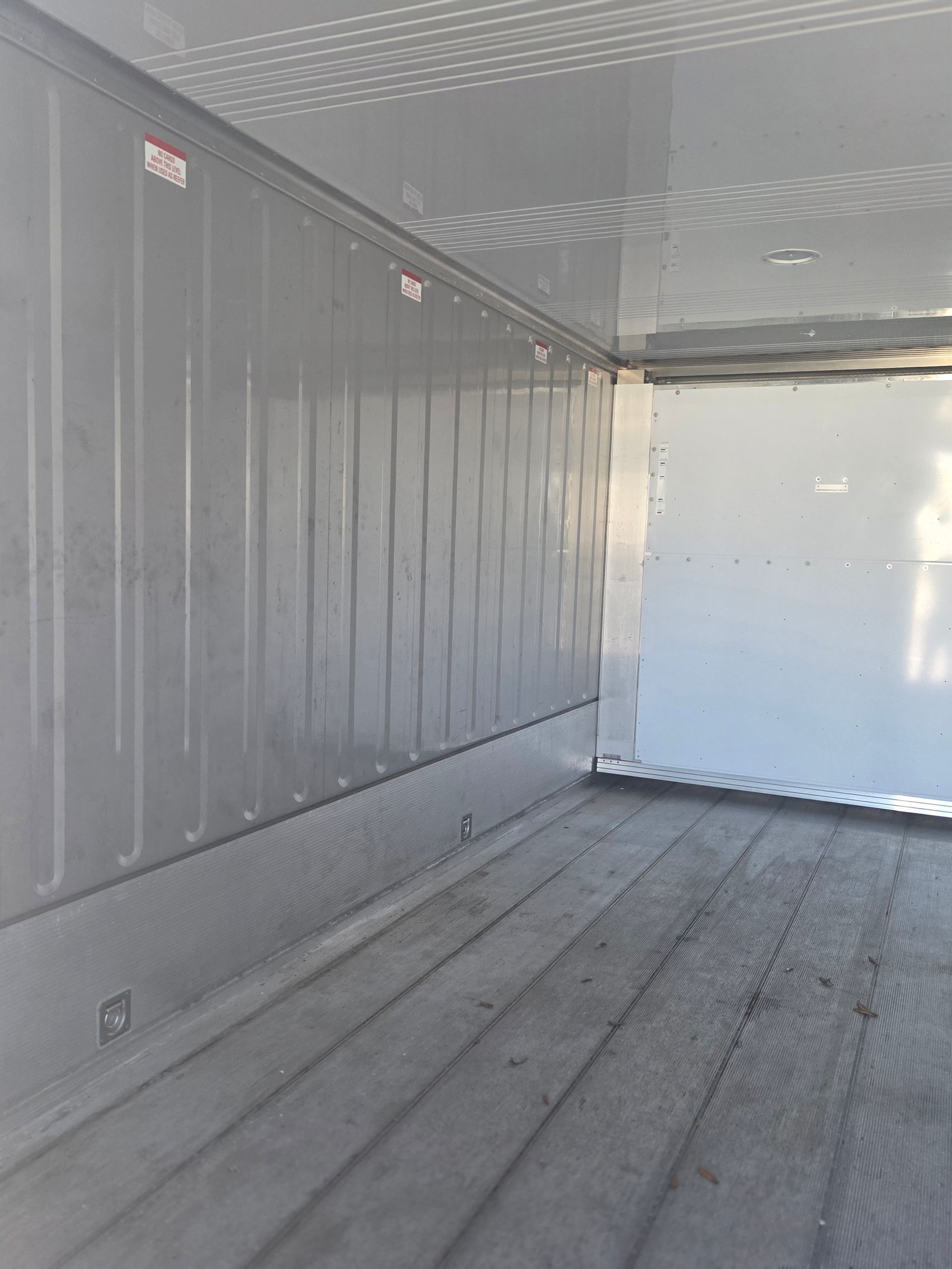 Interior view of an empty white truck trailer with ribbed walls and a wooden floor.