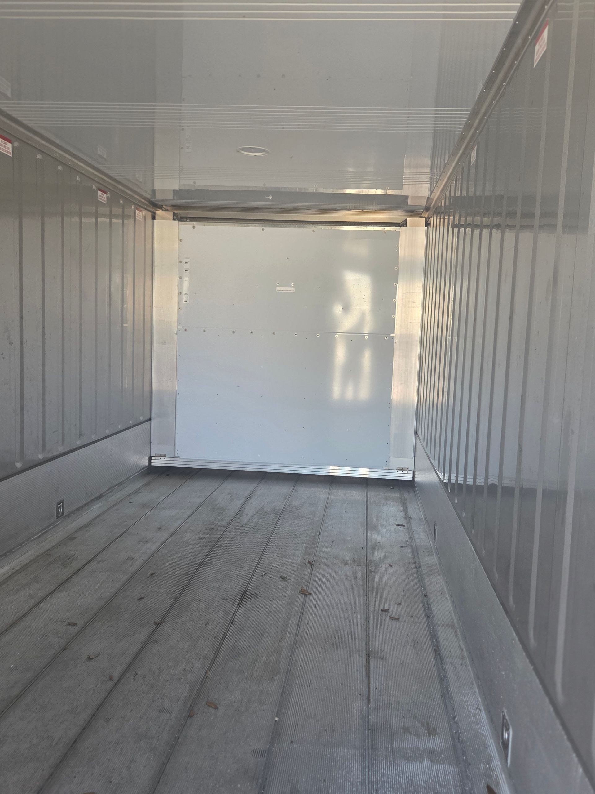 Empty, gray cargo container interior with wooden floorboards and a closed door.