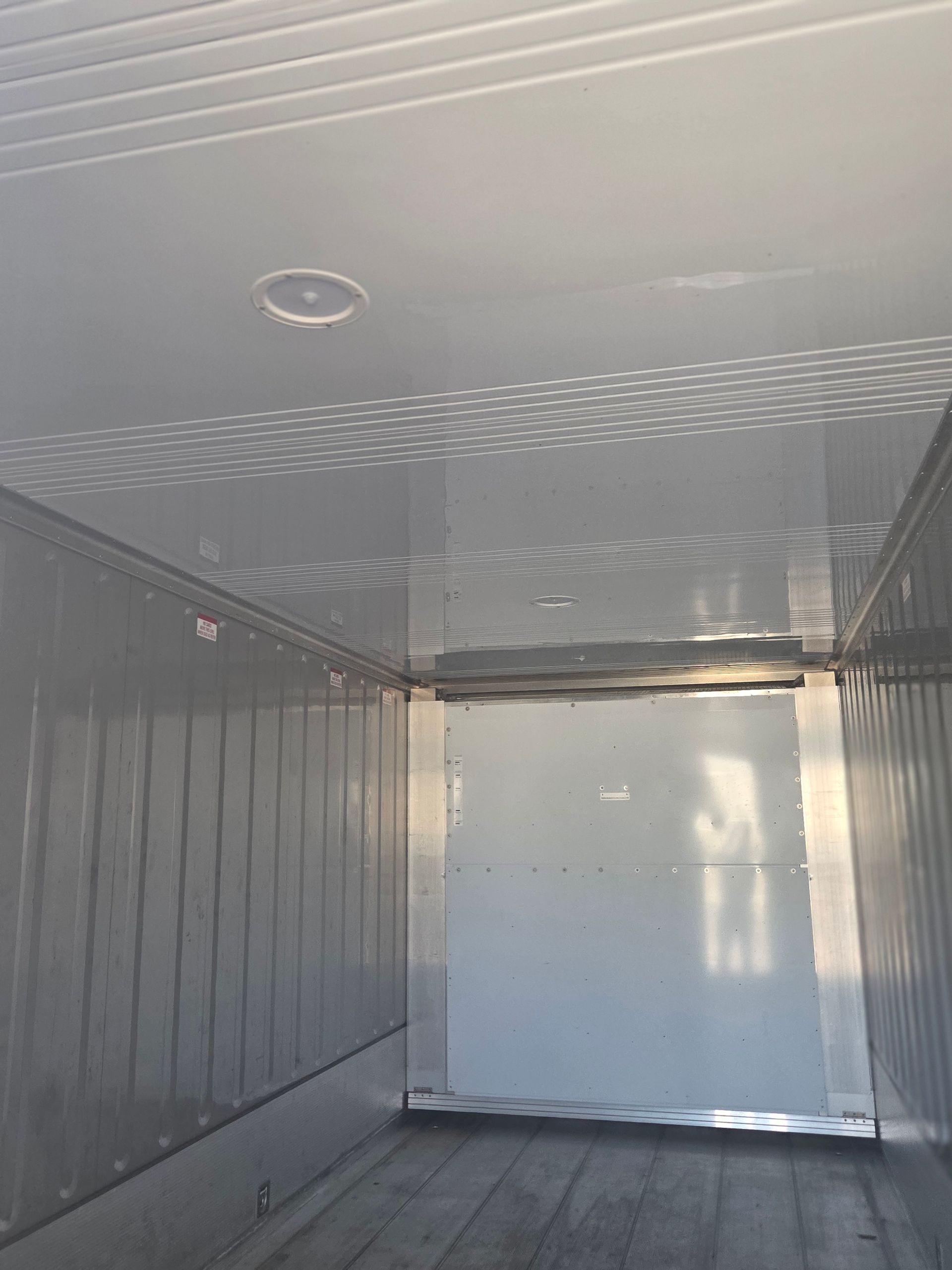 Inside of an empty white cargo trailer, showing ceiling, walls, and door.