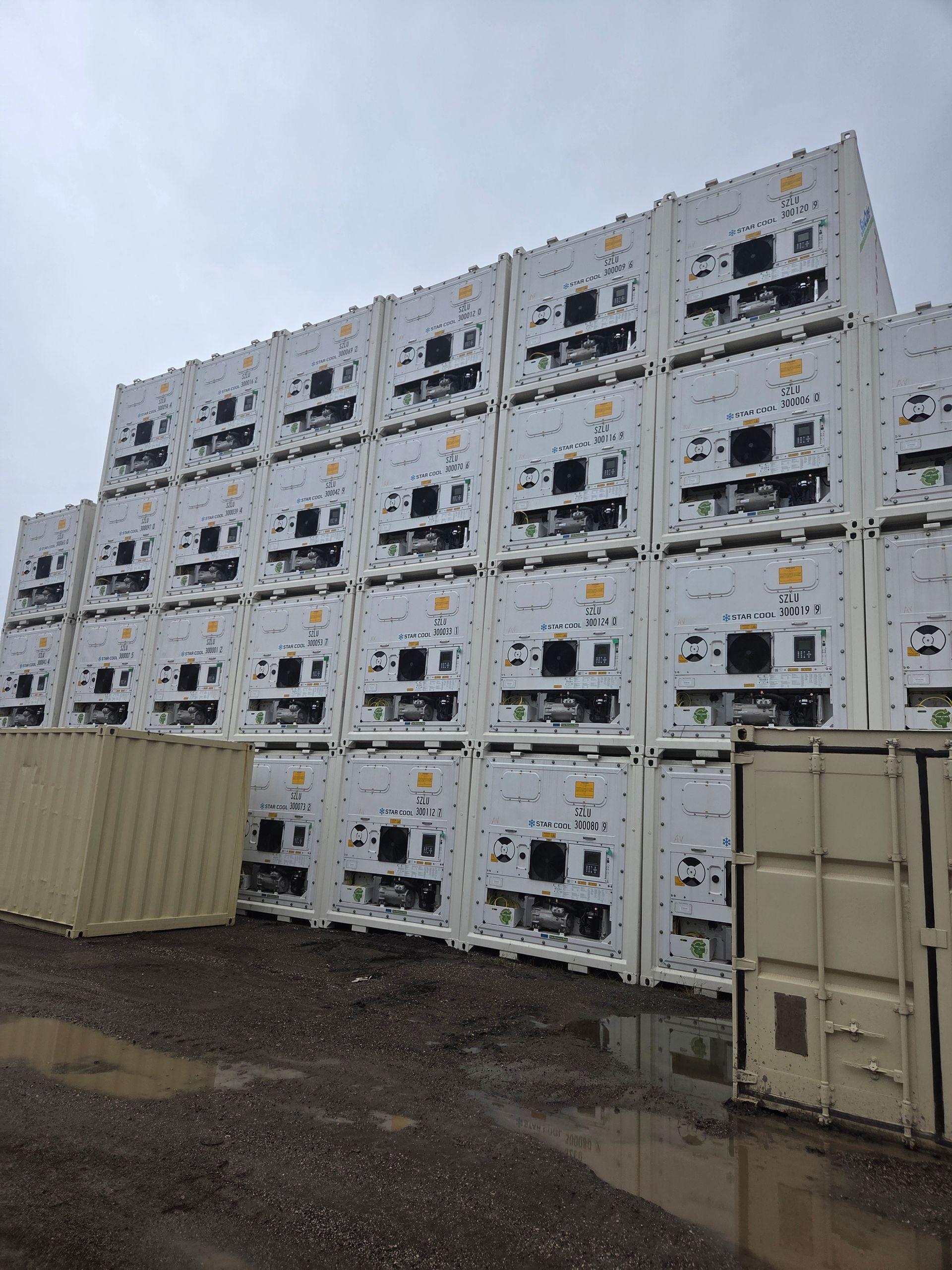 Stack of white refrigerated shipping containers in an outdoor lot on an overcast day.