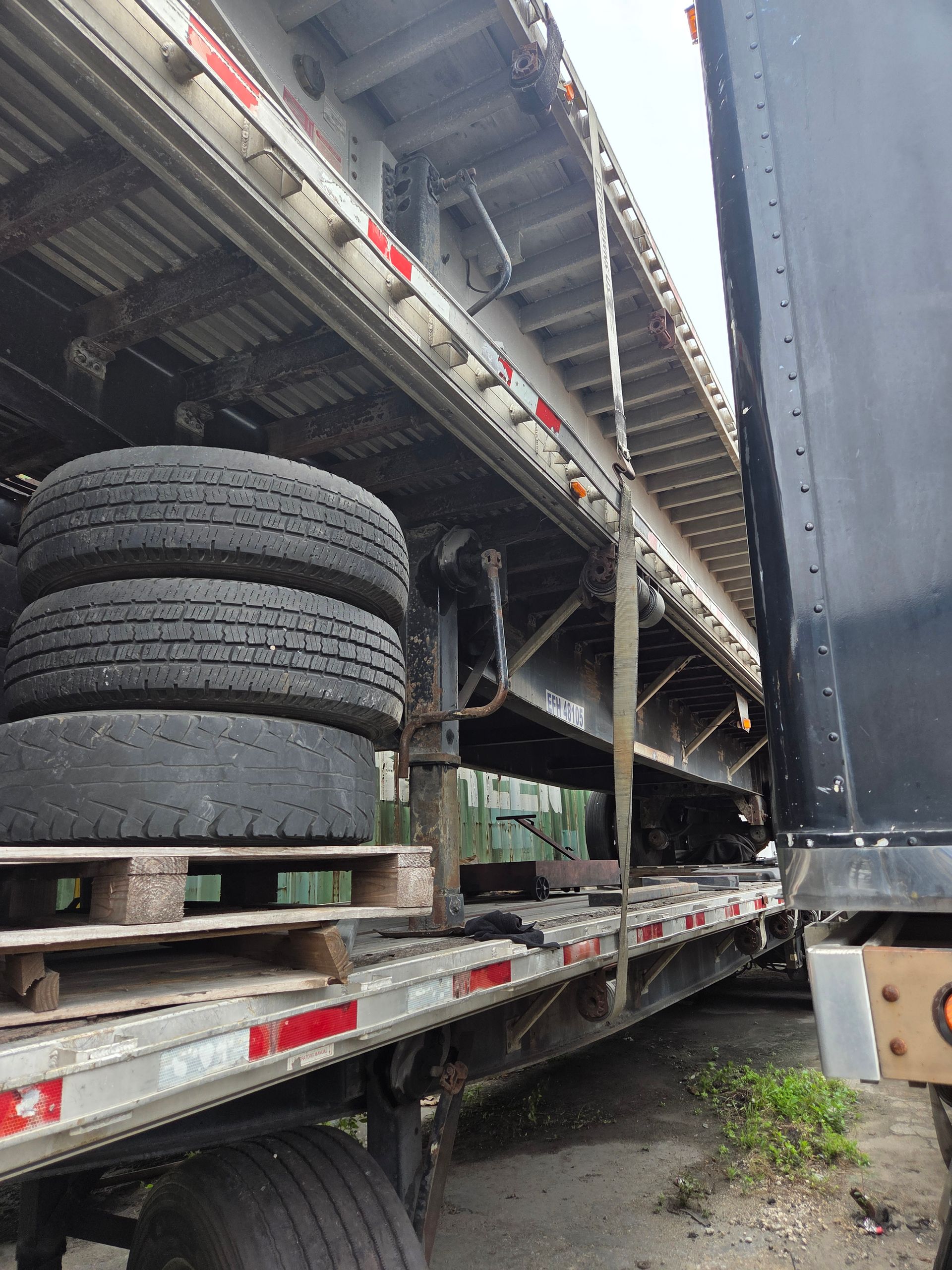 Tires stacked on a pallet inside an open semi-trailer. The trailer is parked outside on a gray day.