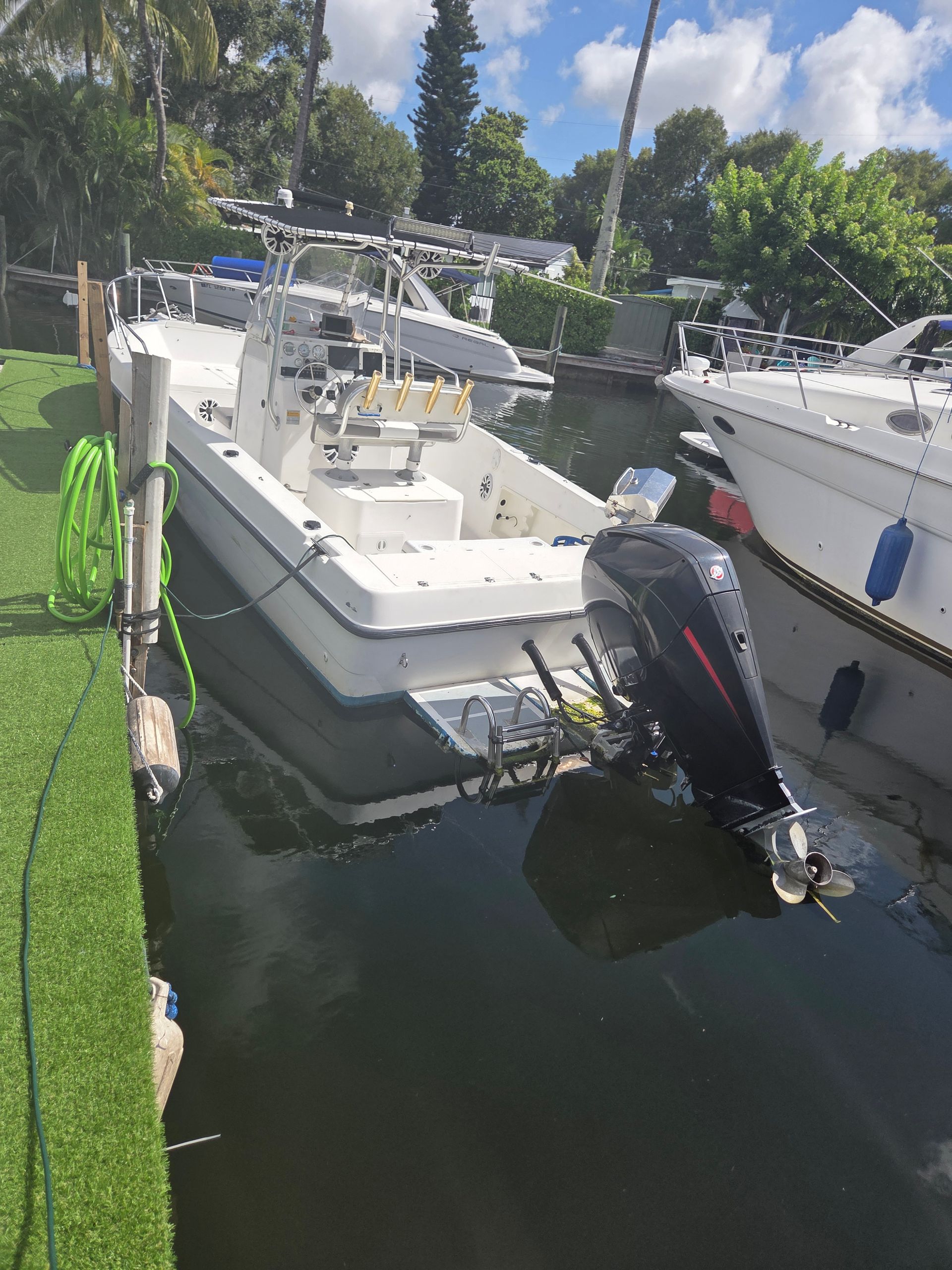 White motorboat docked in canal, black outboard motor, green hose, other boats in background.