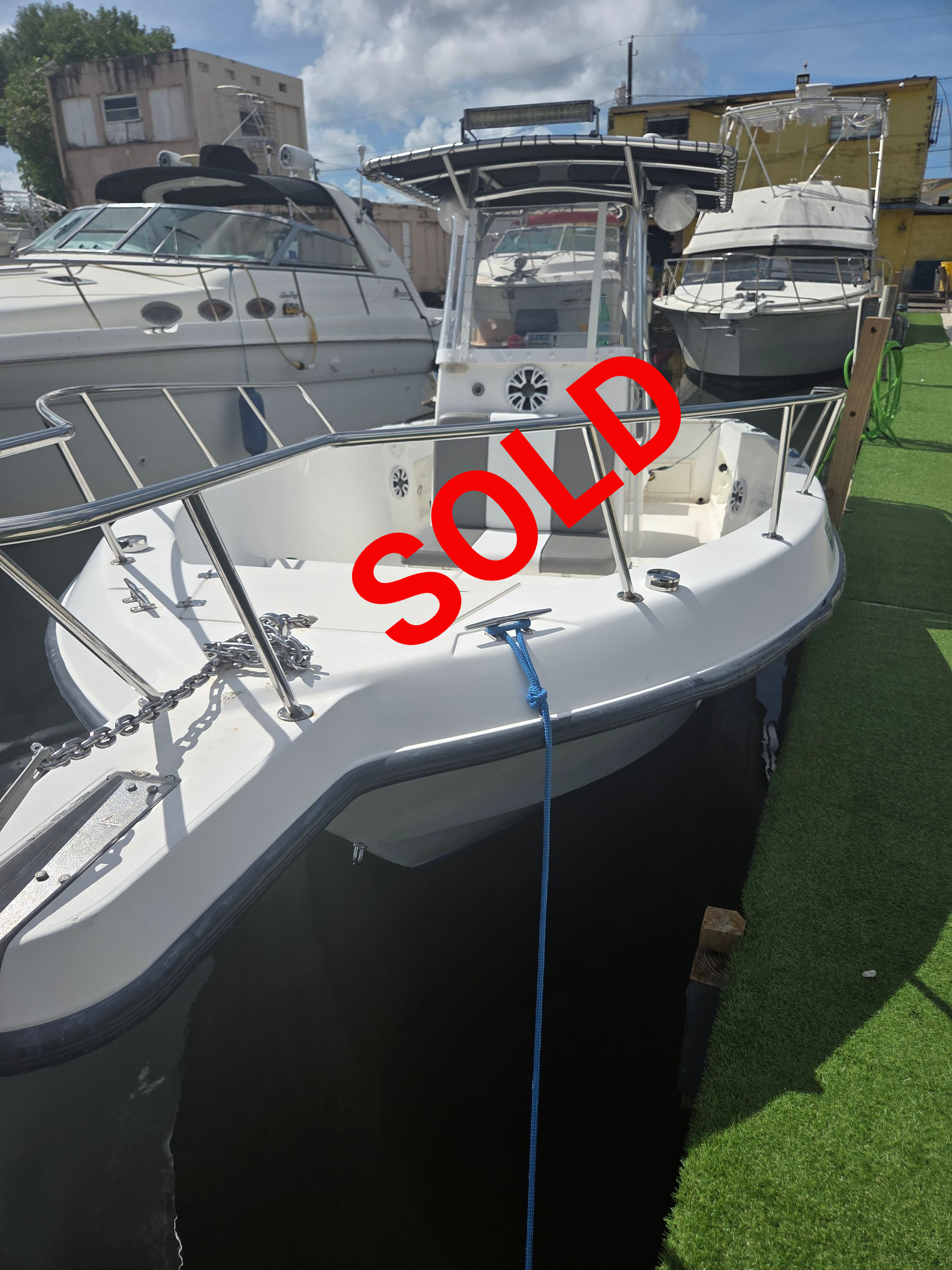 White boat with center console docked, surrounded by other boats and green grass.