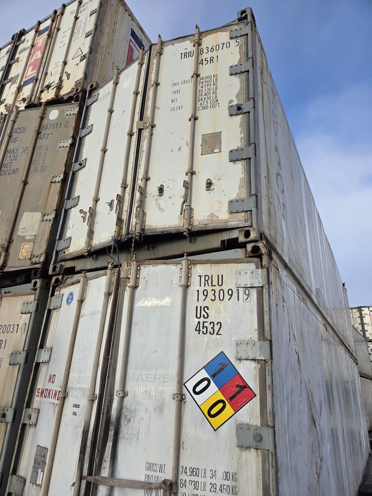 Stacked, white shipping containers with metal details. A hazardous materials diamond is visible.