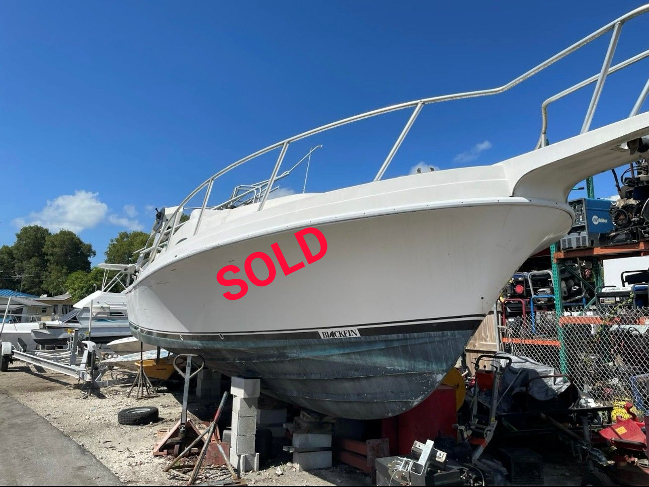 White boat on blocks, outdoors. Blue hull, white rails, sunny day.