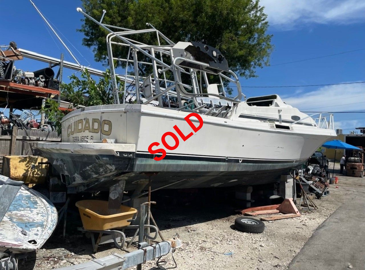 A white boat with black trim on blocks in a junkyard under a blue sky.