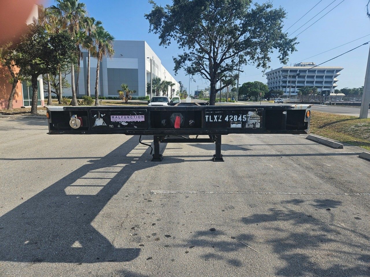 Empty black shipping container chassis in parking lot.