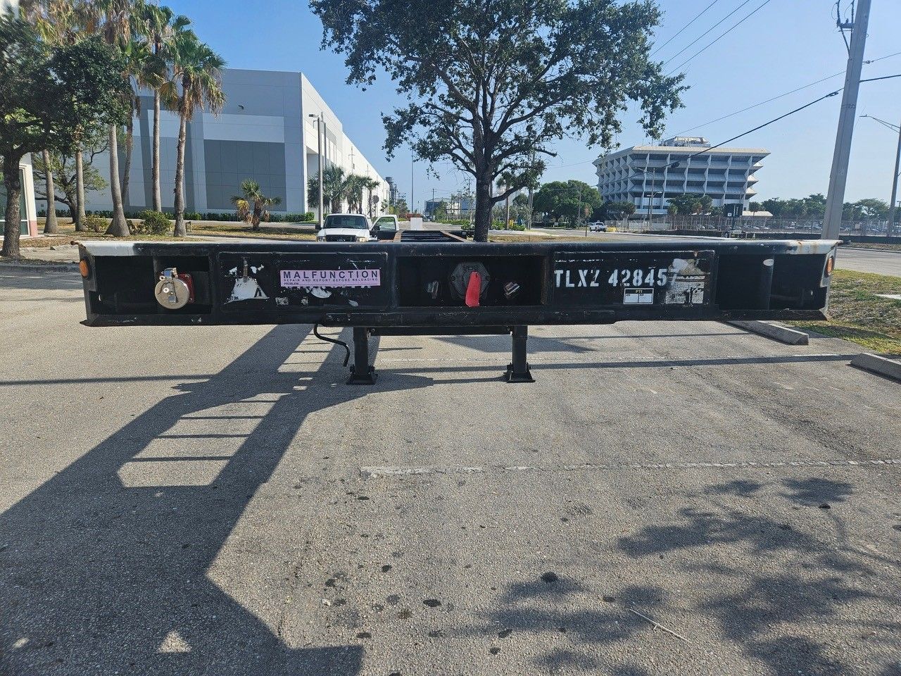 Black trailer frame in a parking lot, with a blurry background of buildings and trees.