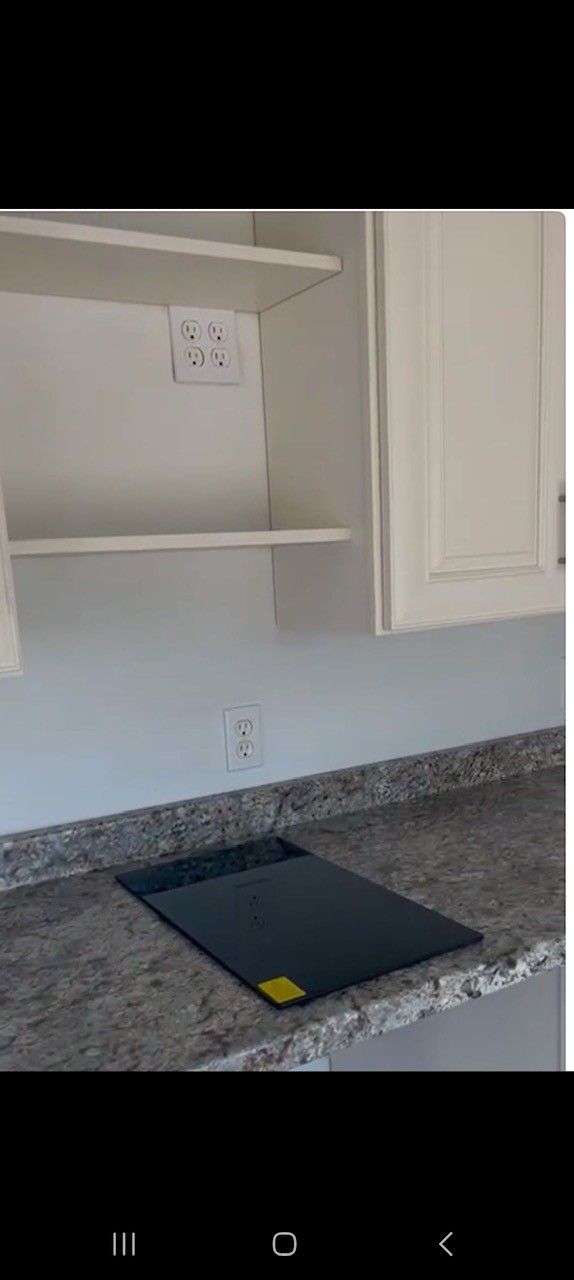 Kitchen counter with built-in stovetop. White cabinets and granite countertop. Wall outlet.