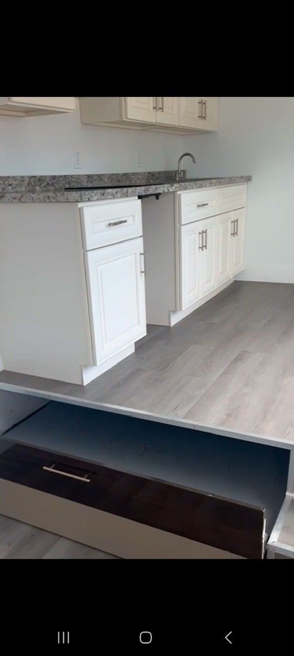 White kitchen cabinets with a gray countertop and a sink. Gray flooring.
