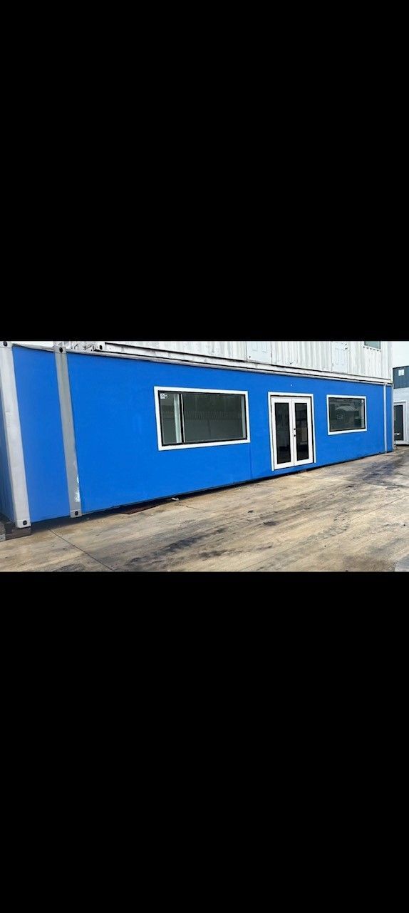Blue modular building with windows and double doors on a gravel lot.