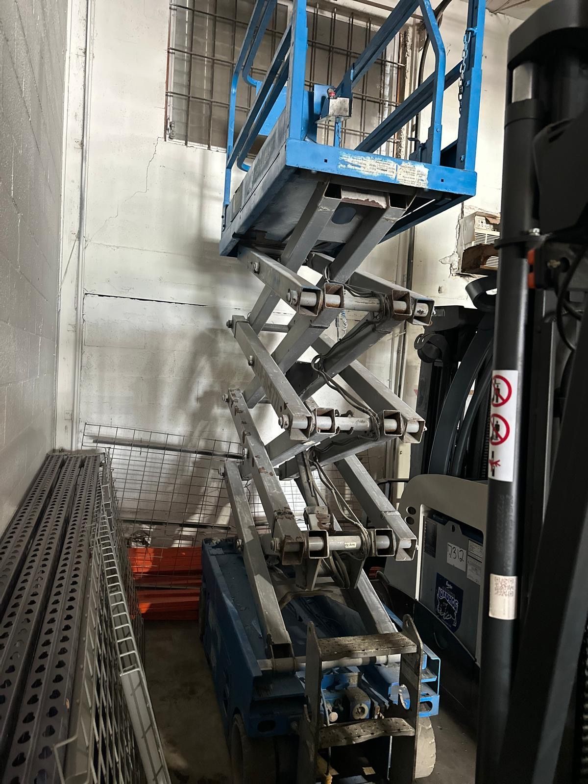 Blue scissor lift in a storage area.