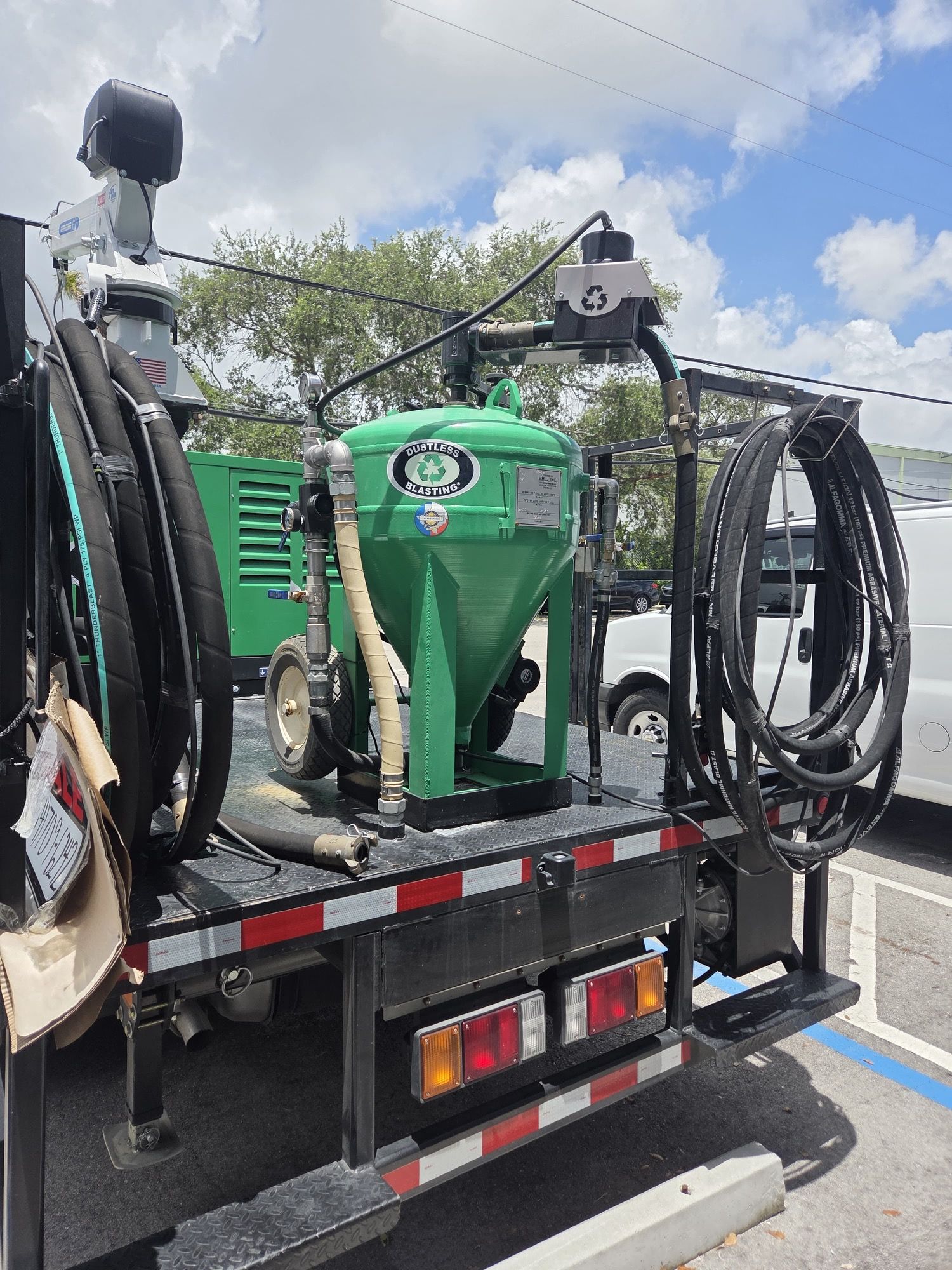 Green sandblasting machine mounted on a truck bed, under a blue sky.