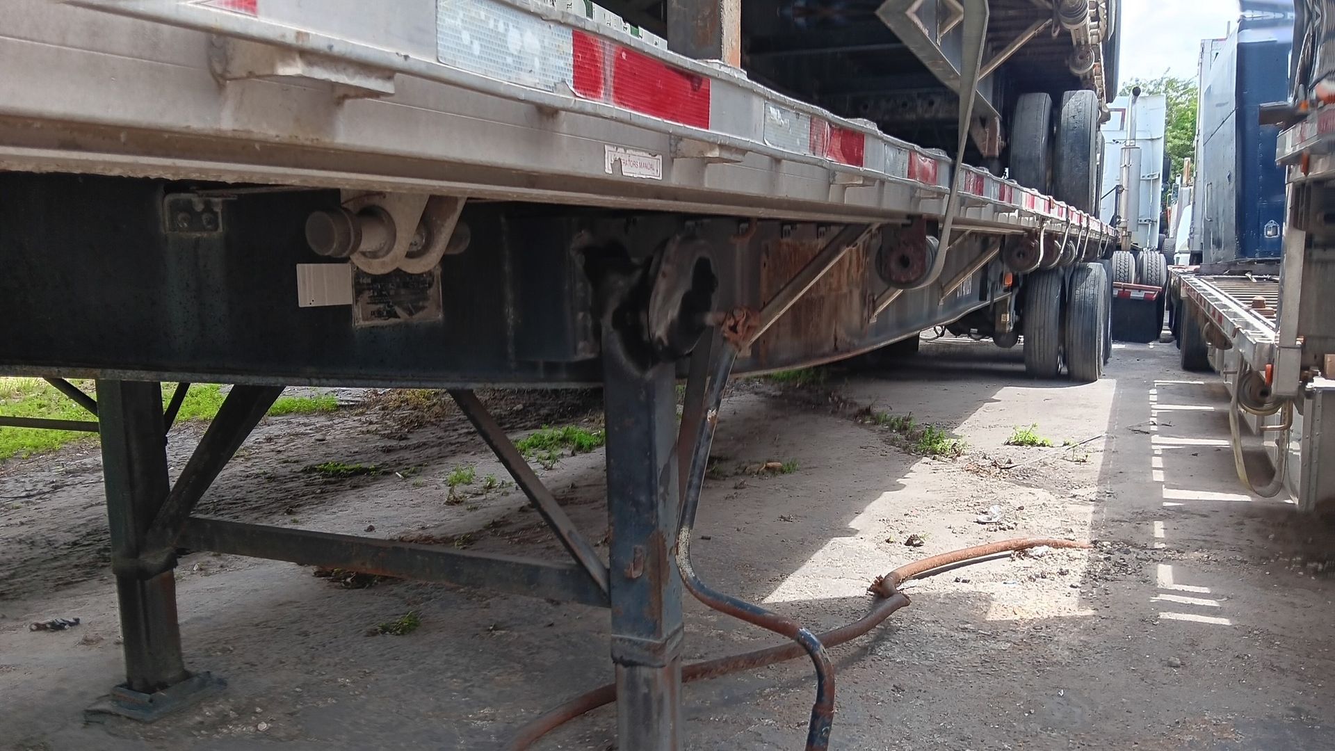 Semi-trailer hitch and support stand, outdoors. Steel construction, on asphalt, with other trailers nearby.