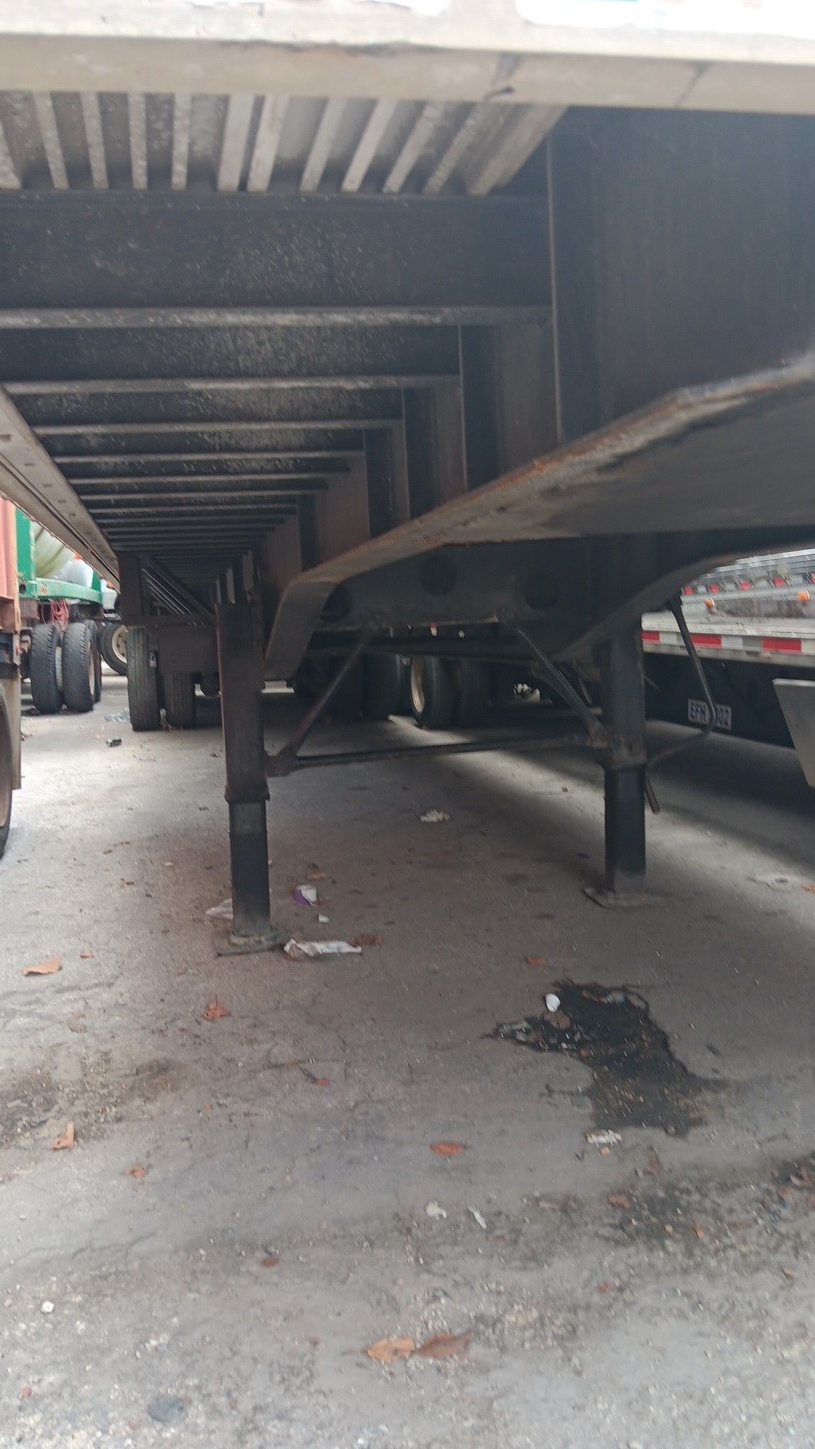 Underside of a semi-trailer on a concrete surface, with support beams and wheels visible in the background.