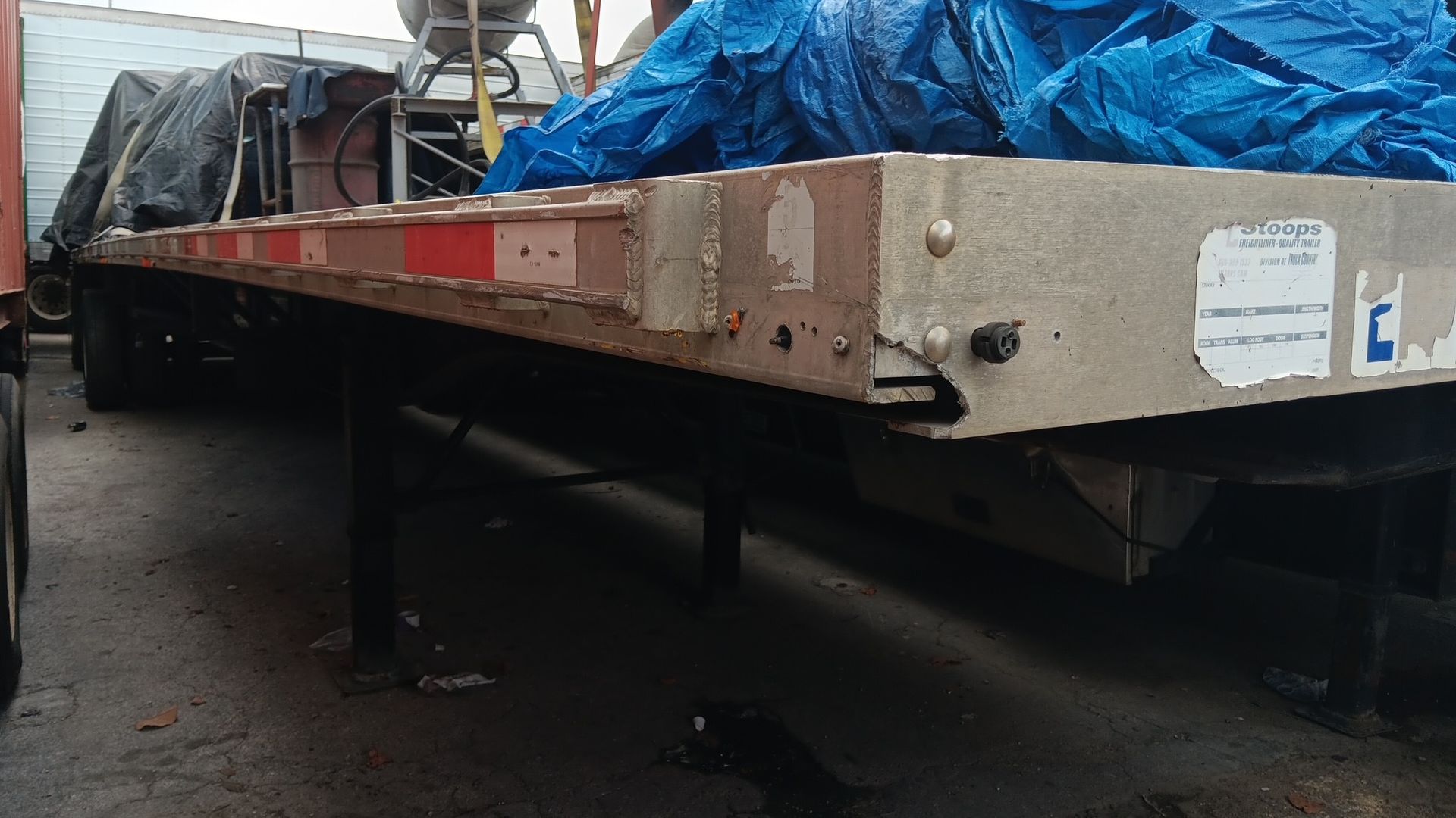 Flatbed trailer with blue tarp covering something, outdoors.