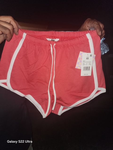 Red shorts with white trim and drawstring, held by hands.