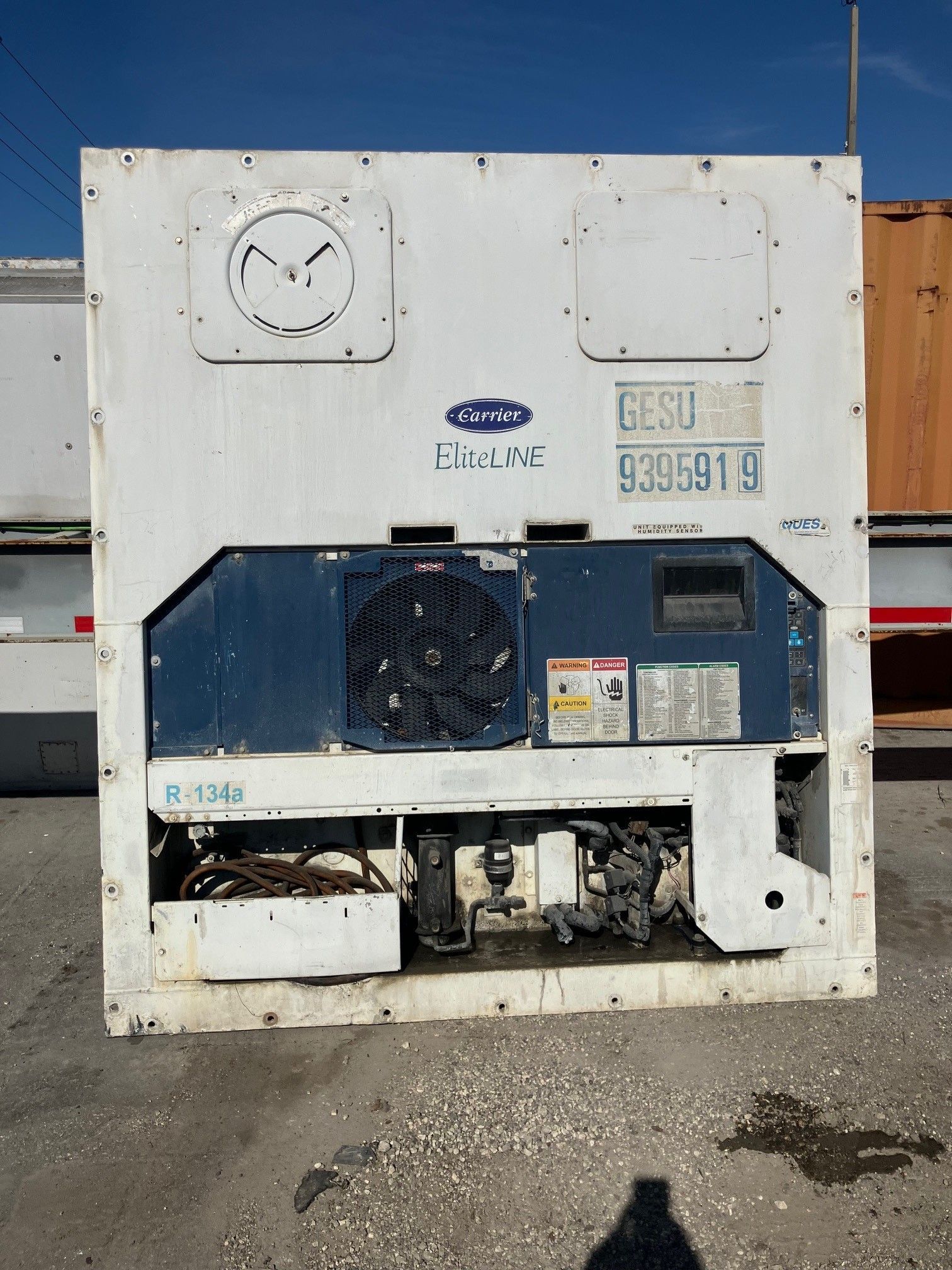 White Carrier reefer unit with blue components and a large fan, outdoors.