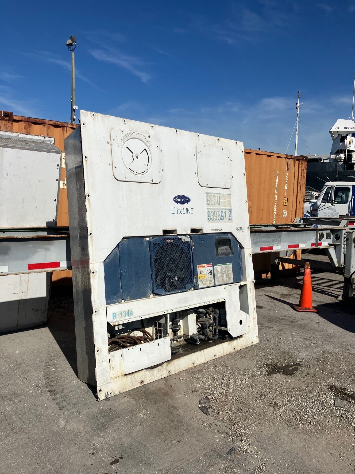 White Carrier refrigeration unit on a trailer, with a blue accent, on a paved surface under a blue sky.