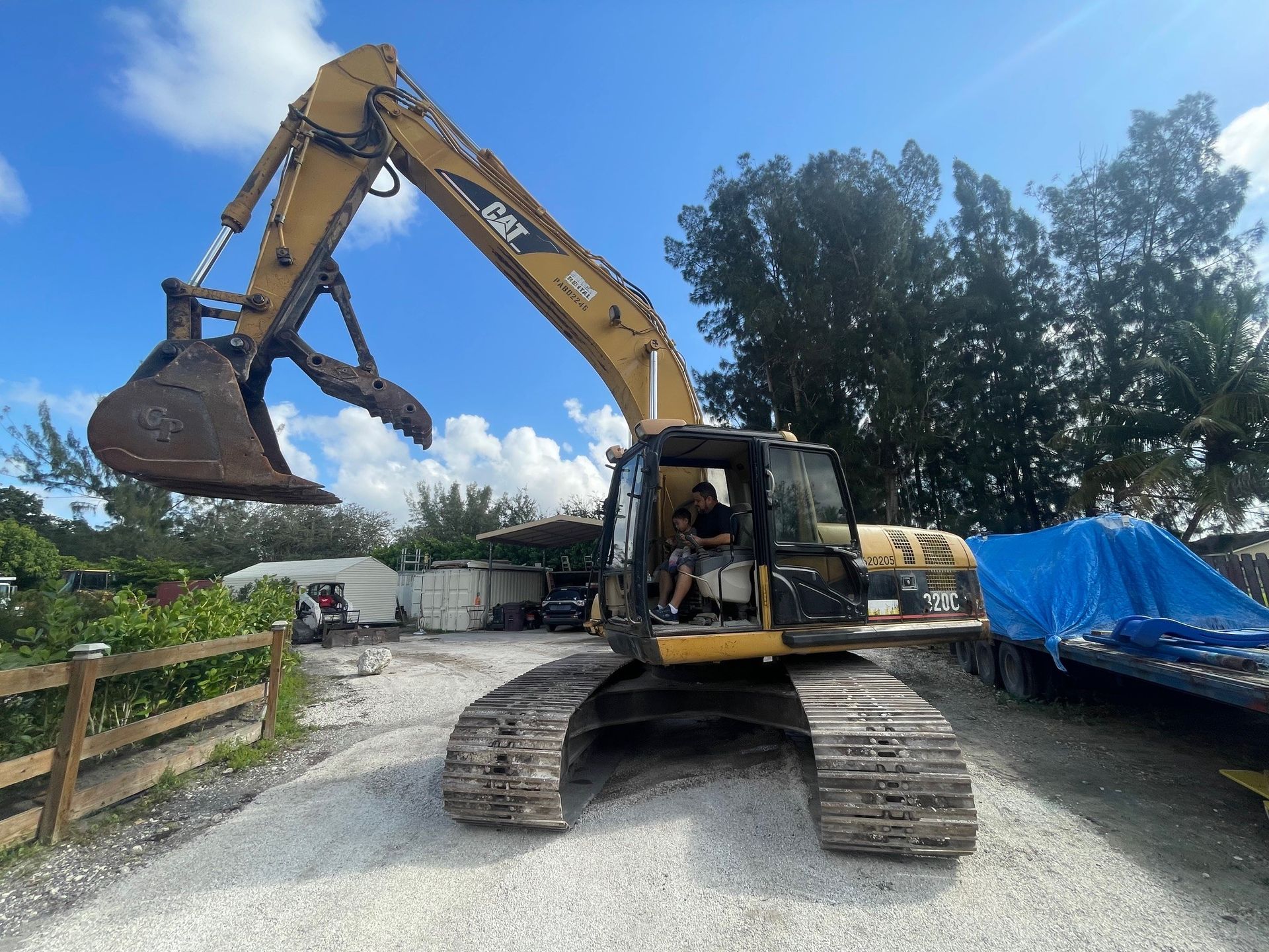Yellow Caterpillar excavator with grapple arm raised, on gravel, against a cloudy sky.