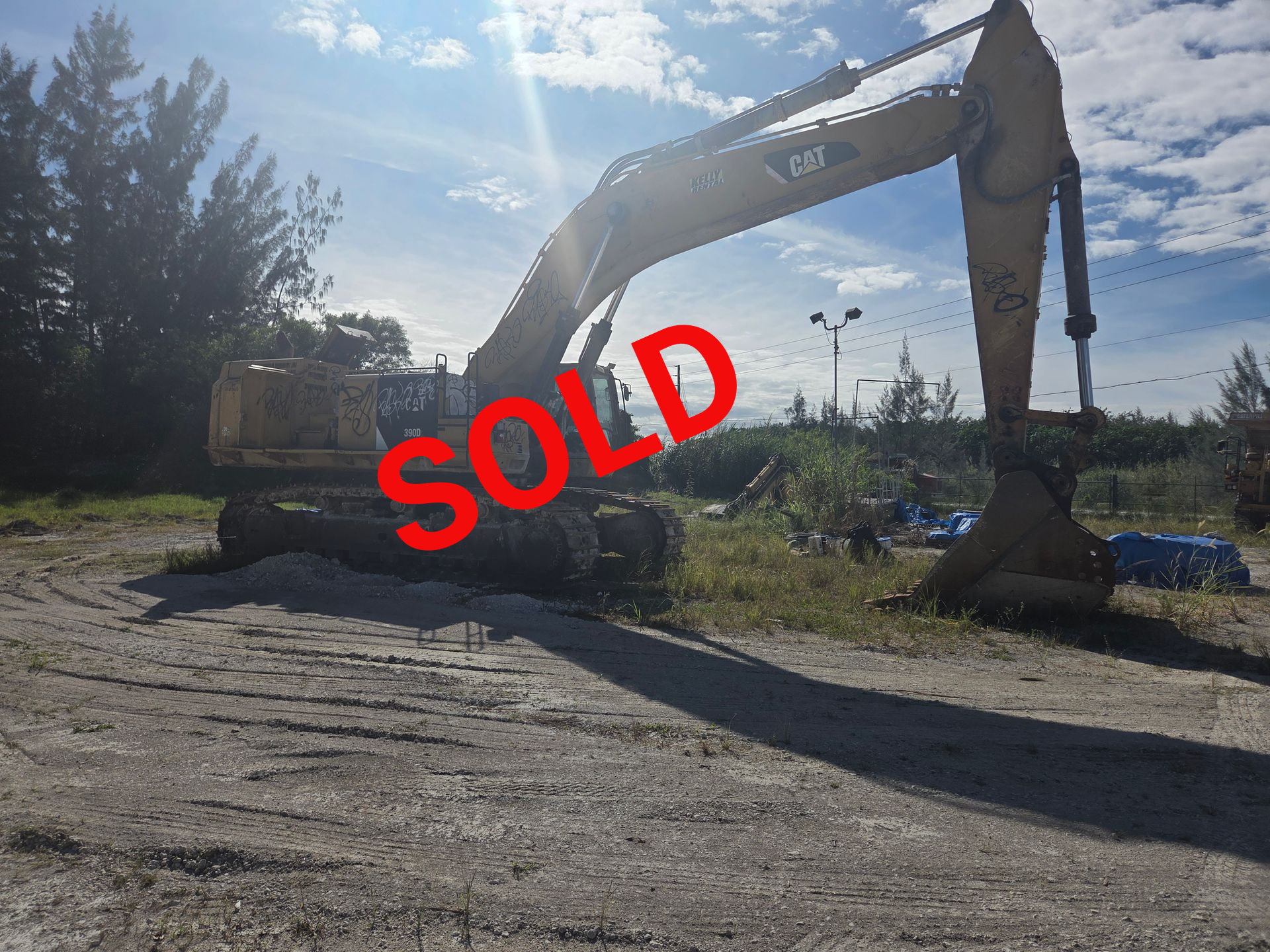 A yellow Caterpillar excavator on a dirt lot under a bright sky.