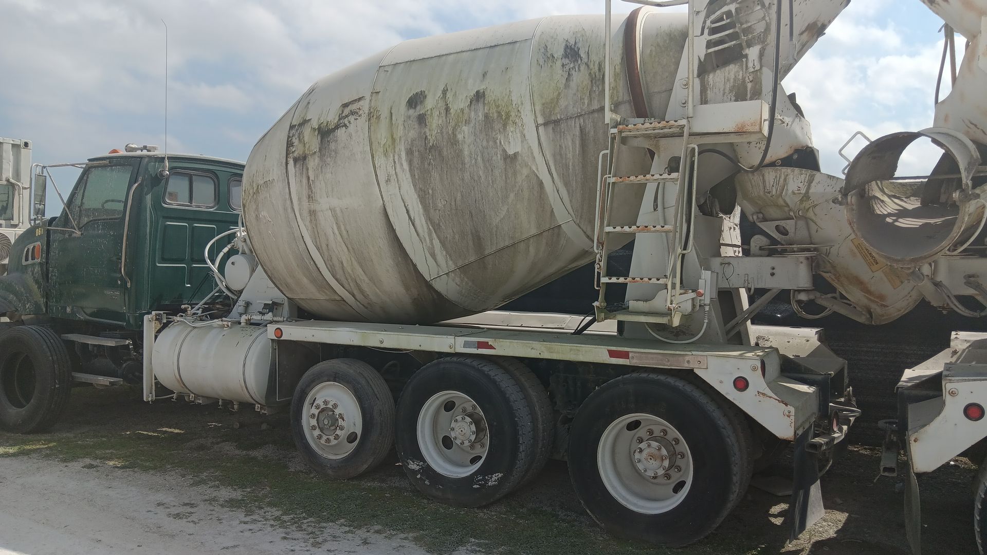 Green and white concrete mixer truck parked outdoors.