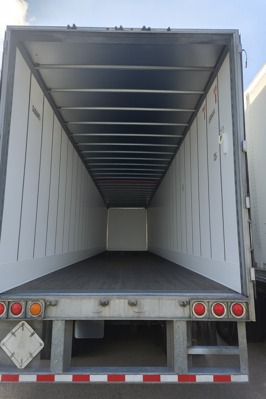 Interior of an empty white semi-trailer. Gray metal roof and floor with white side panels. Rear bumper with lights.