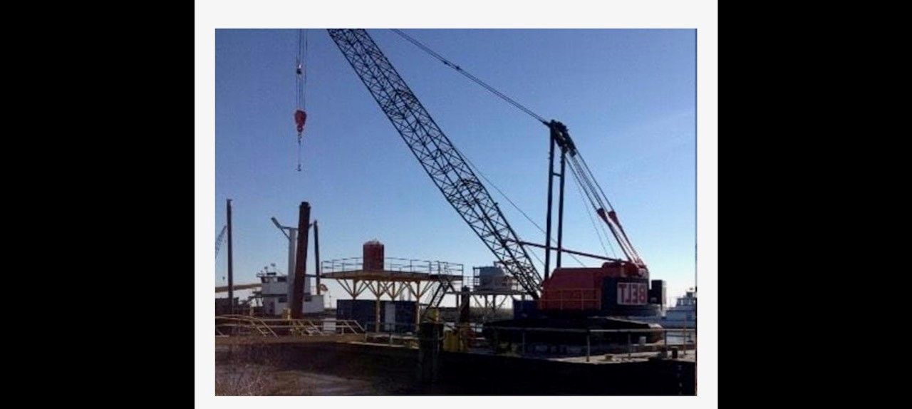 A large construction crane lifting something near a structure on a sunny day.