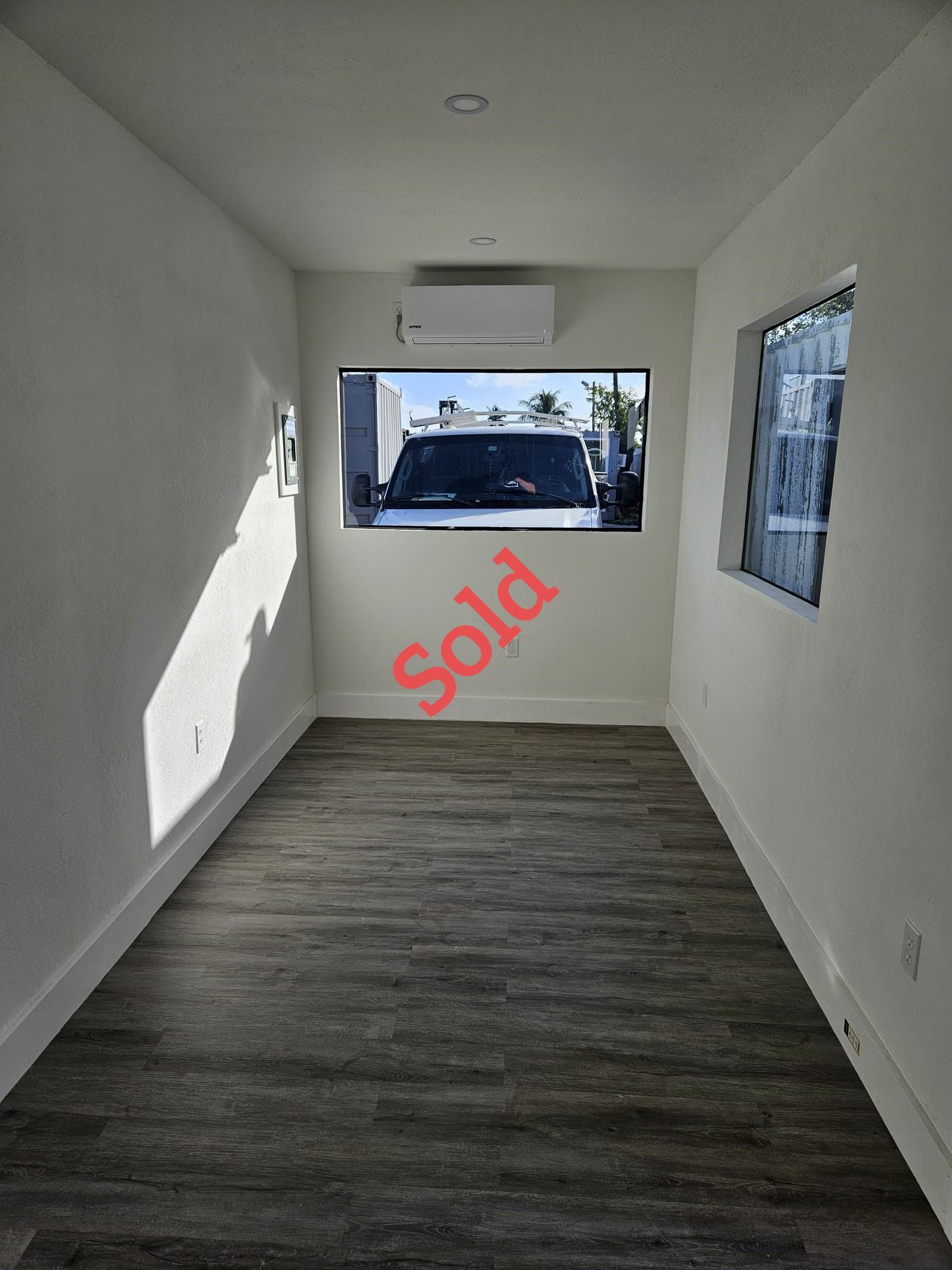 Interior of a room with a large window and wood-look flooring; 